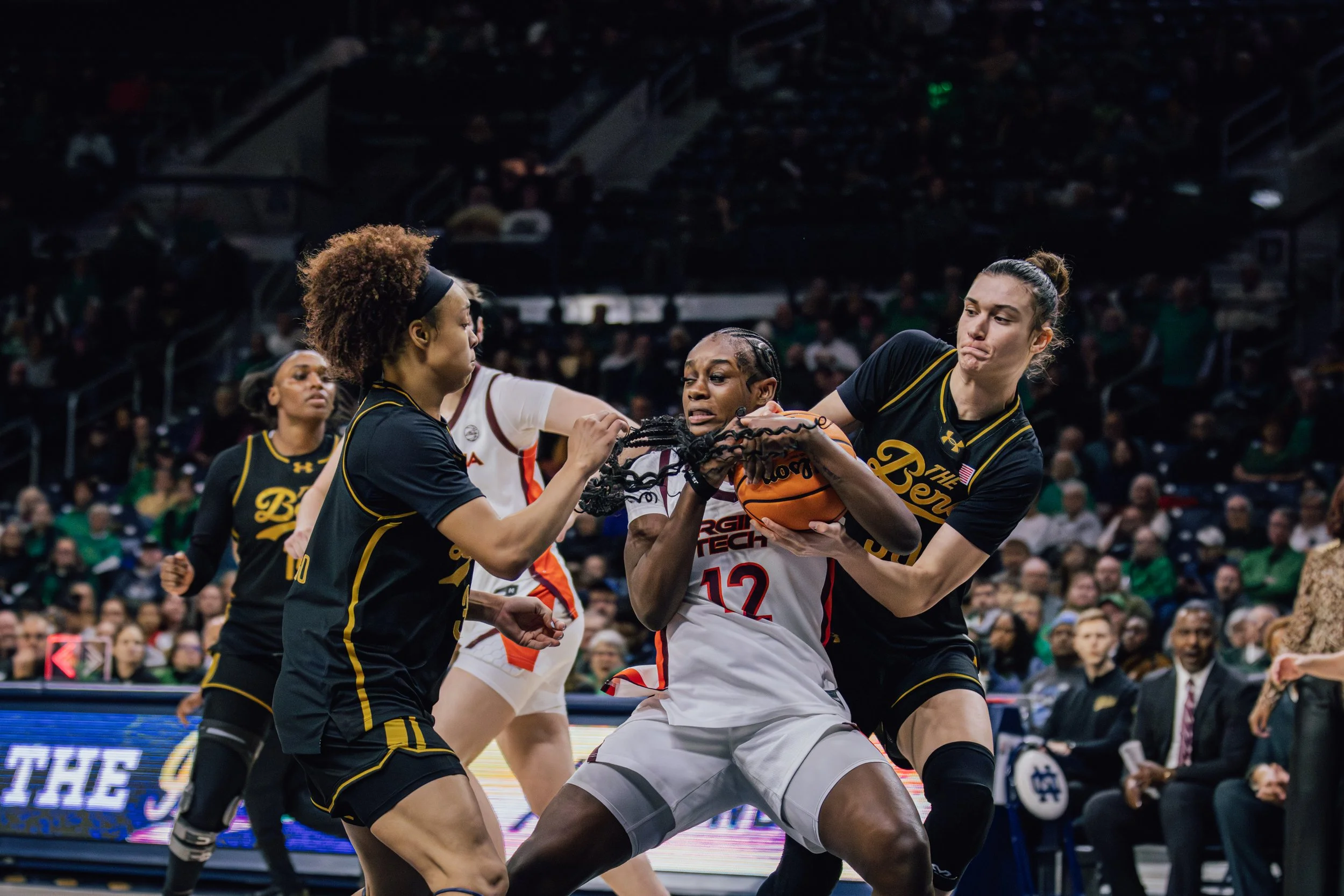 Female basketball players fighting for the ball during a game with a crowd in the background.