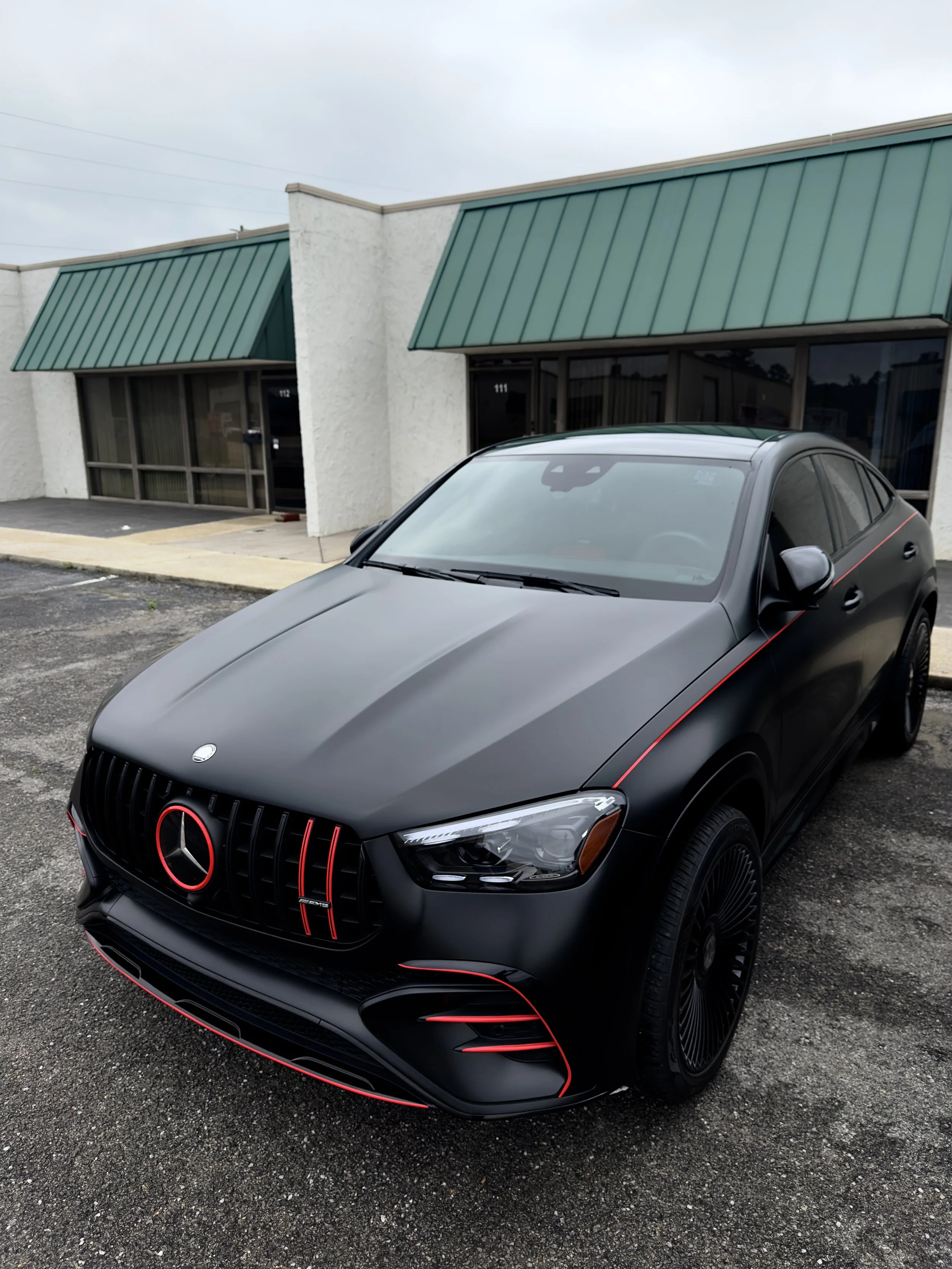 Black Mercedes-Benz car with red accent lines parked outside a building with white walls and green awnings.