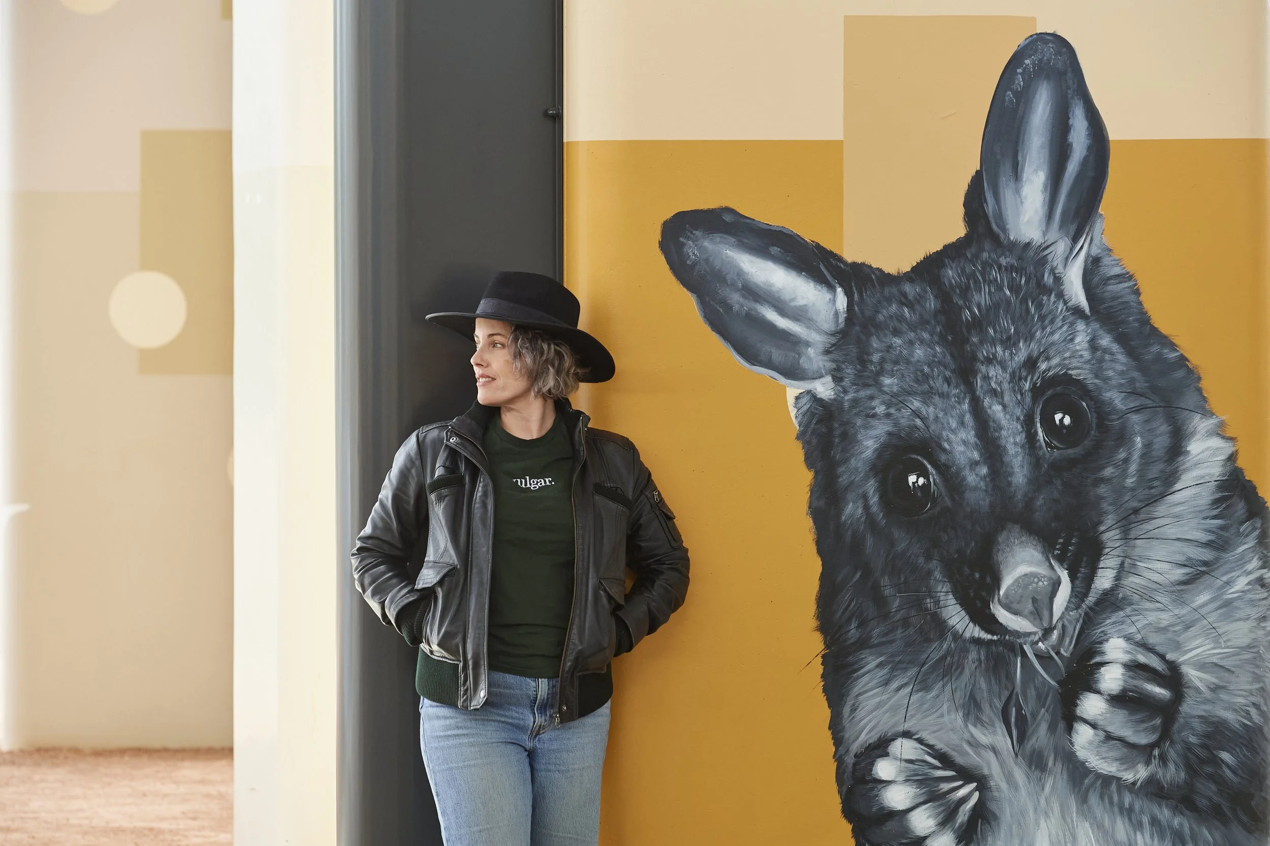 Fieldey, the artist posing next to a hand-painted possum mural, highlighting large-scale mural practice and contemporary public art.