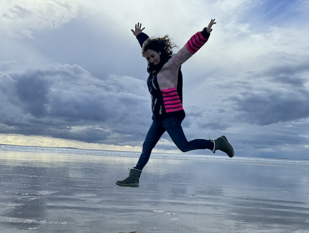 A silhouette background banner of a woman leaping joyfully on a beach, inviting mothers to step into their next chapter and book a discovery call.