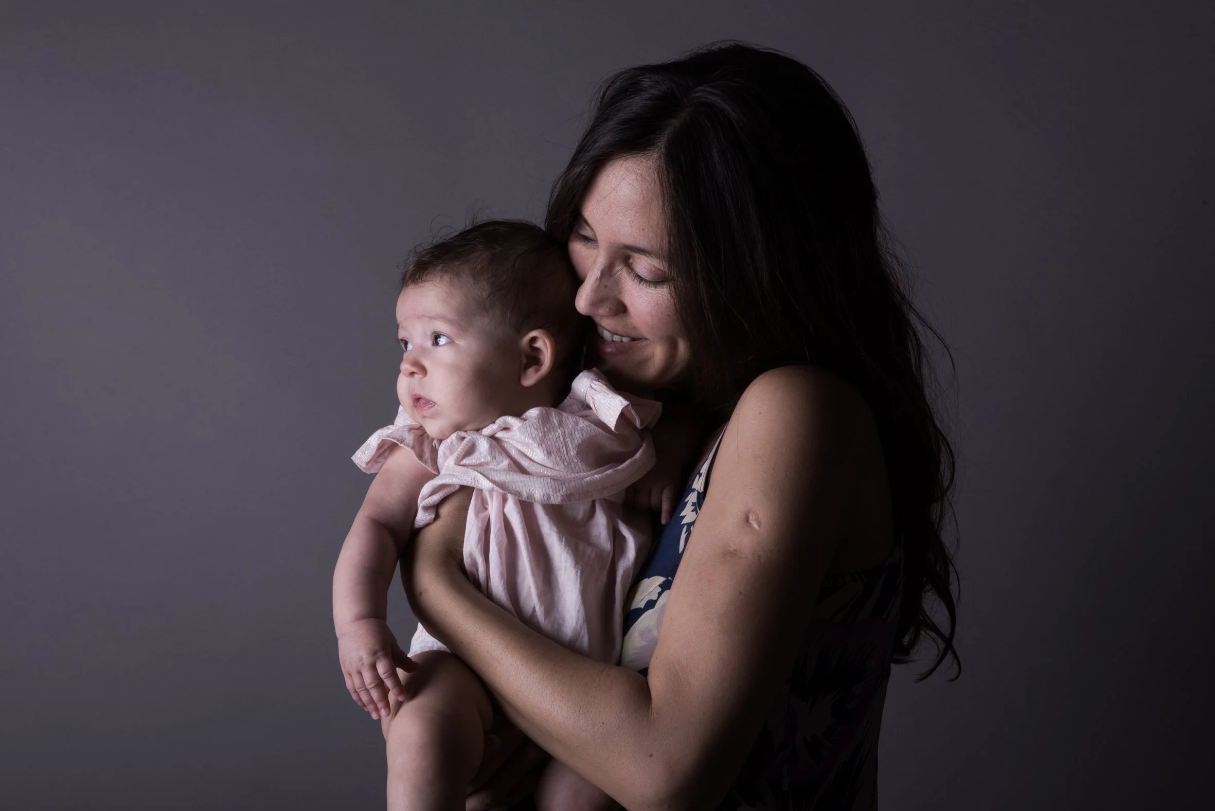 A warm studio portrait of a mother holding her baby girl, setting a supportive tone for women transitioning back to work after maternity leave.