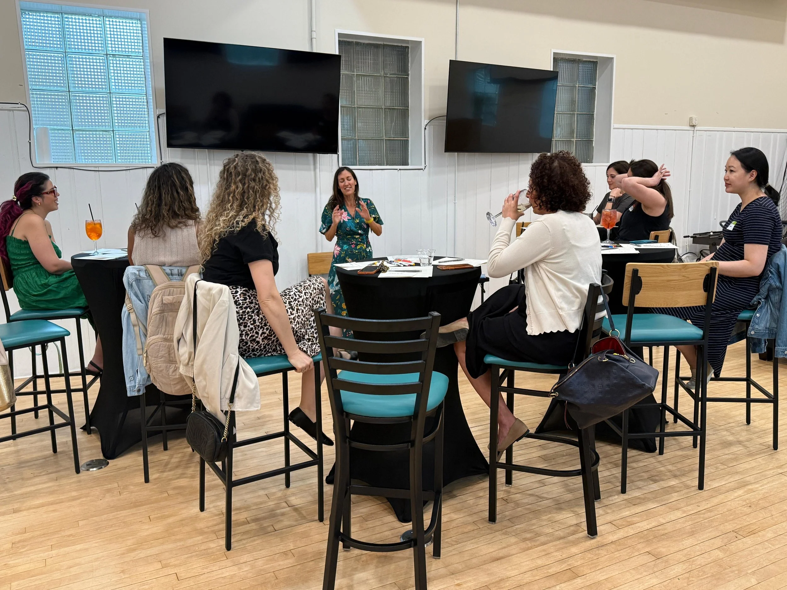 Andi Salcedo facilitating an interactive group discussion at high-top tables inside an event space in Hoboken New Jersey