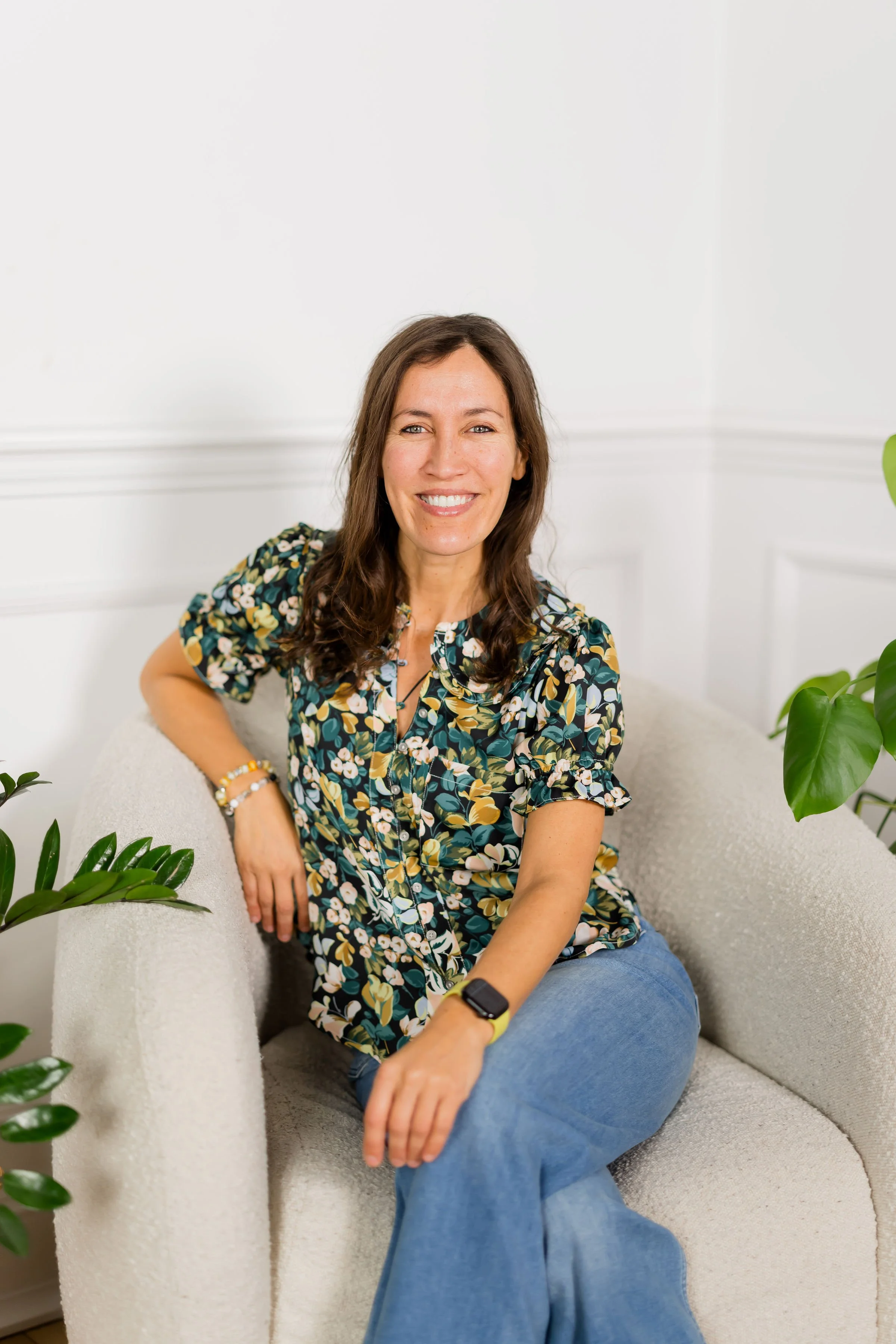 Andi Salcedo, an ICF-certified coach, sitting comfortably in a modern white chair and smiling, representing professional coaching for working mothers in Hoboken, New Jersey.