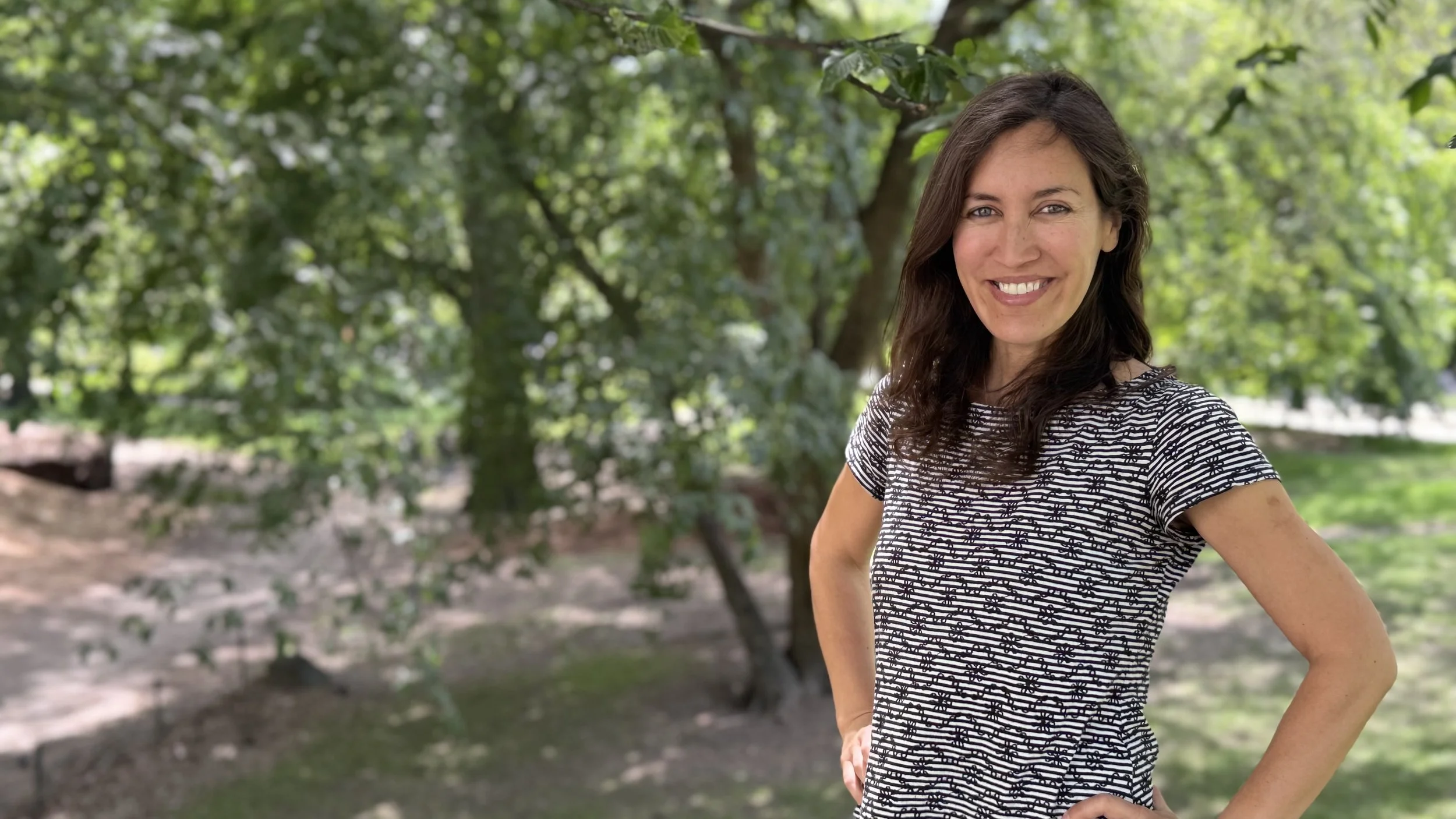 Andi Salcedo, founder of Momtoring and career coach for mothers, smiling in front of lush green trees.