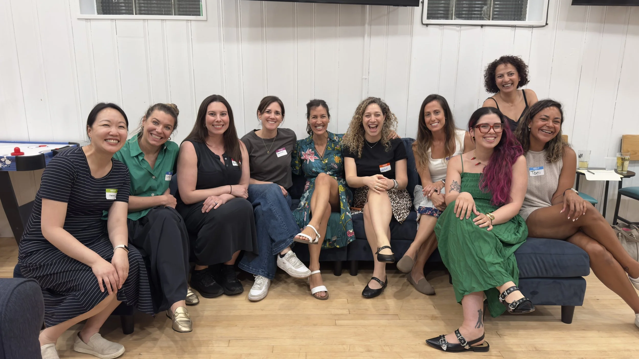 A large group of diverse working mothers smiling and laughing together during a Momtoring community meetup event in Hoboken.