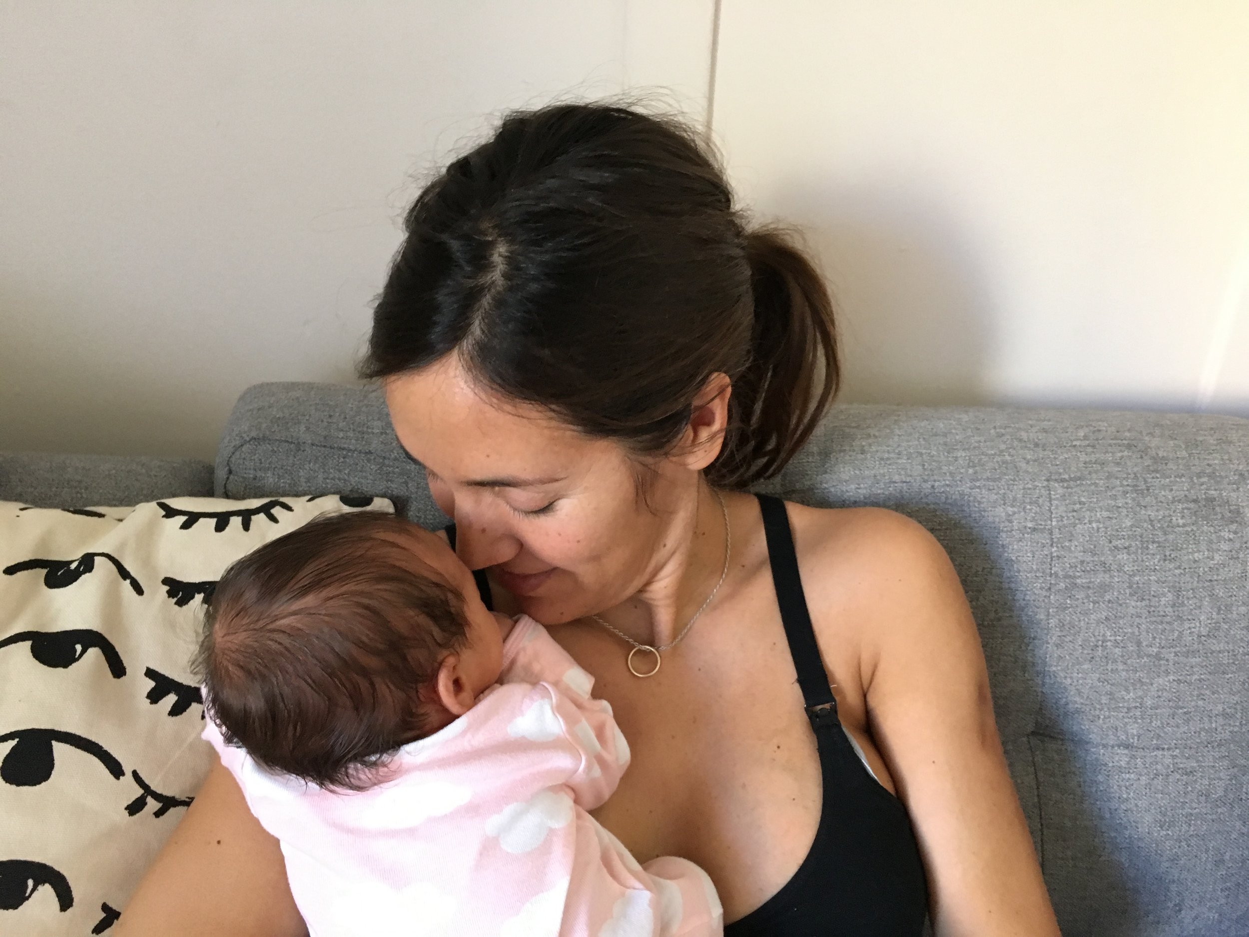 A mother tenderly holding and kissing her newborn baby while sitting on a living room couch, capturing a moment of deep maternal connection.