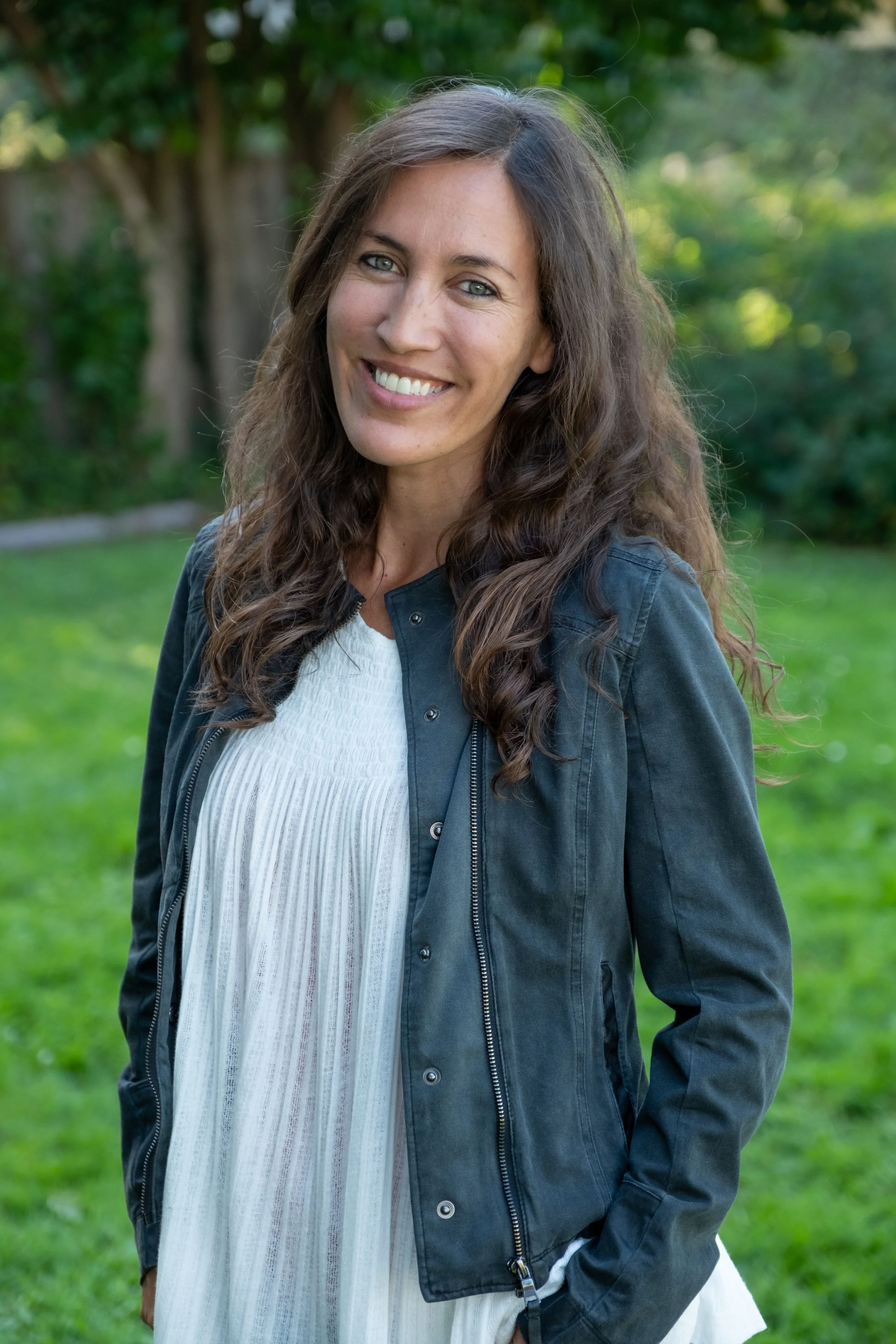 A close-up portrait of life coach Andi Salcedo smiling warmly outdoors, introducing her personal story and coaching philosophy for working mothers.