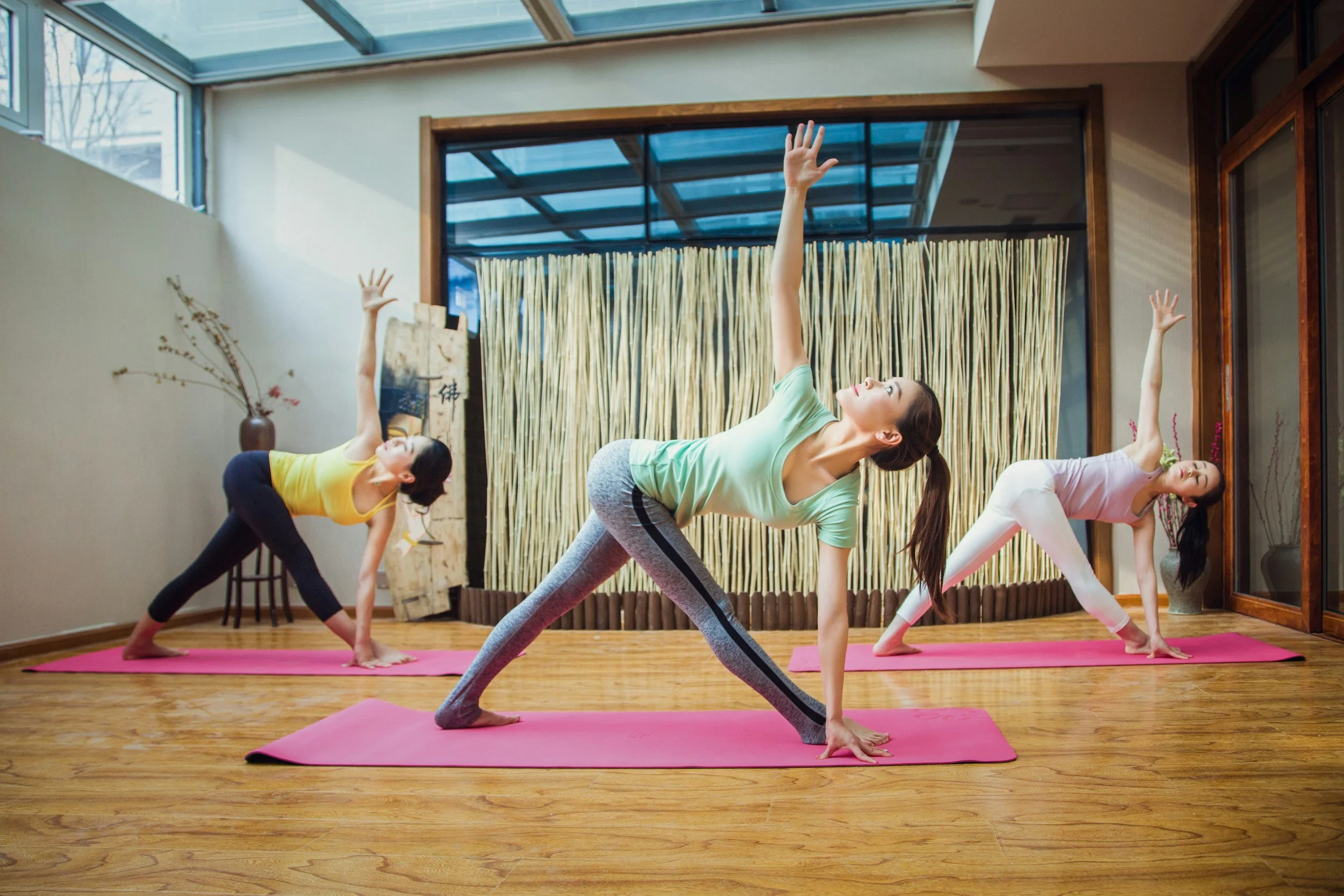 Yoga teacher and two students on the mat in triangle twist pose.