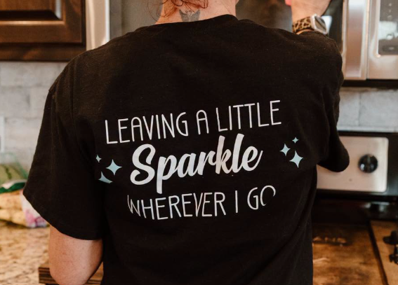 A women in a black shirt with writing on the back, "Leaving a Little Sparking Wherever We Go"