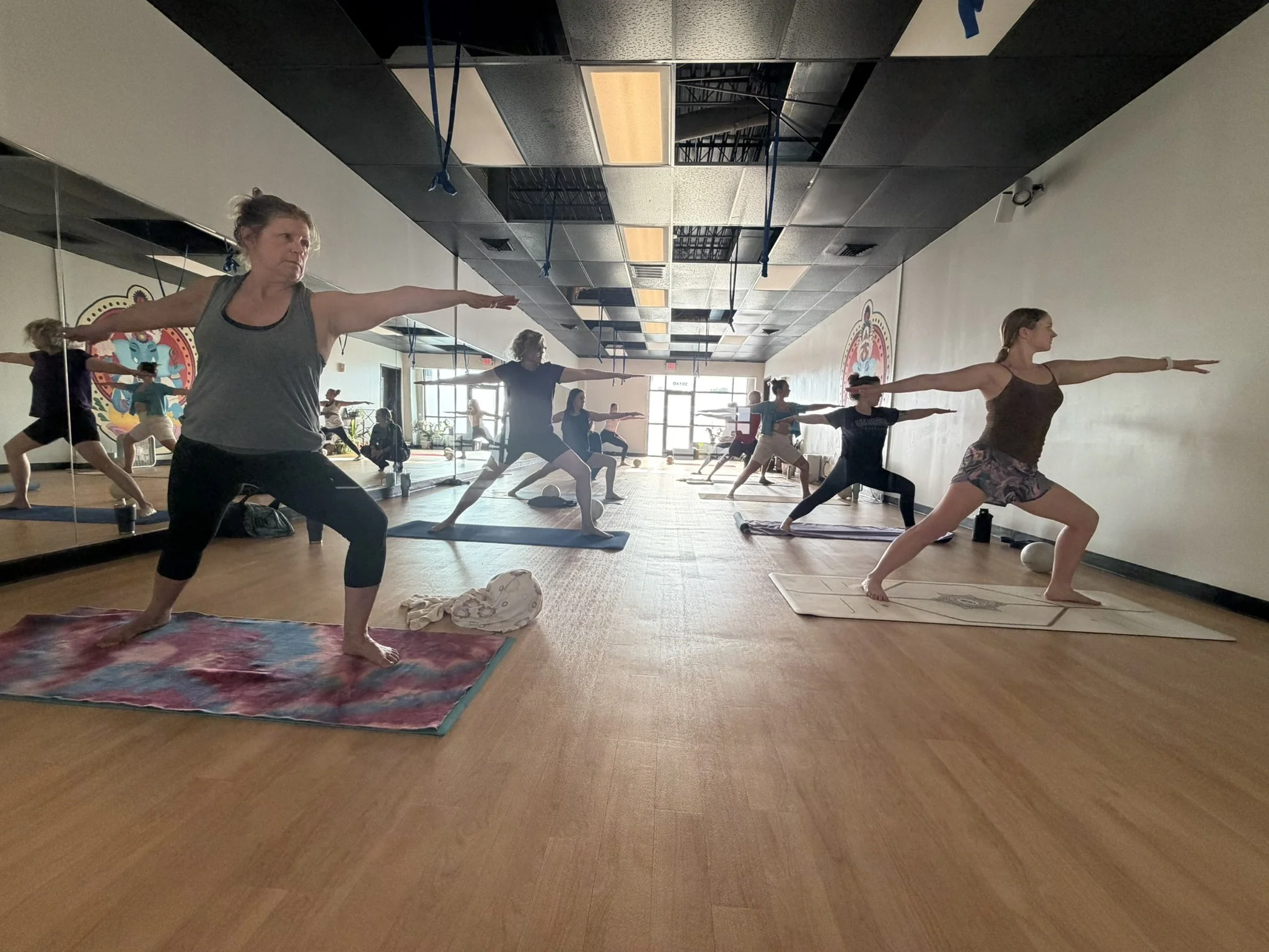 My Hot Yoga Non-Heated room live class of woman in Warrior II.