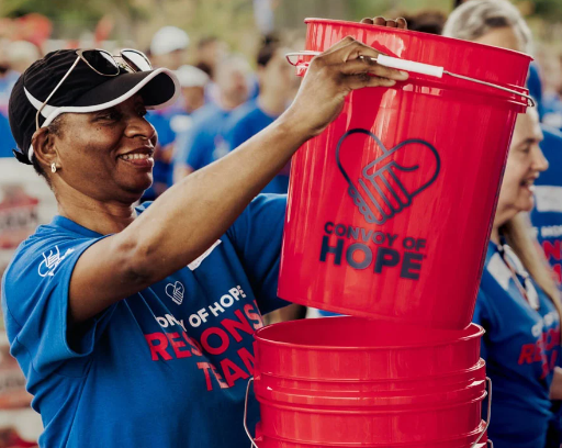 A woman in a blue shirt and baseball copy hoping a red Convoy of Hope 5 gallon bucket