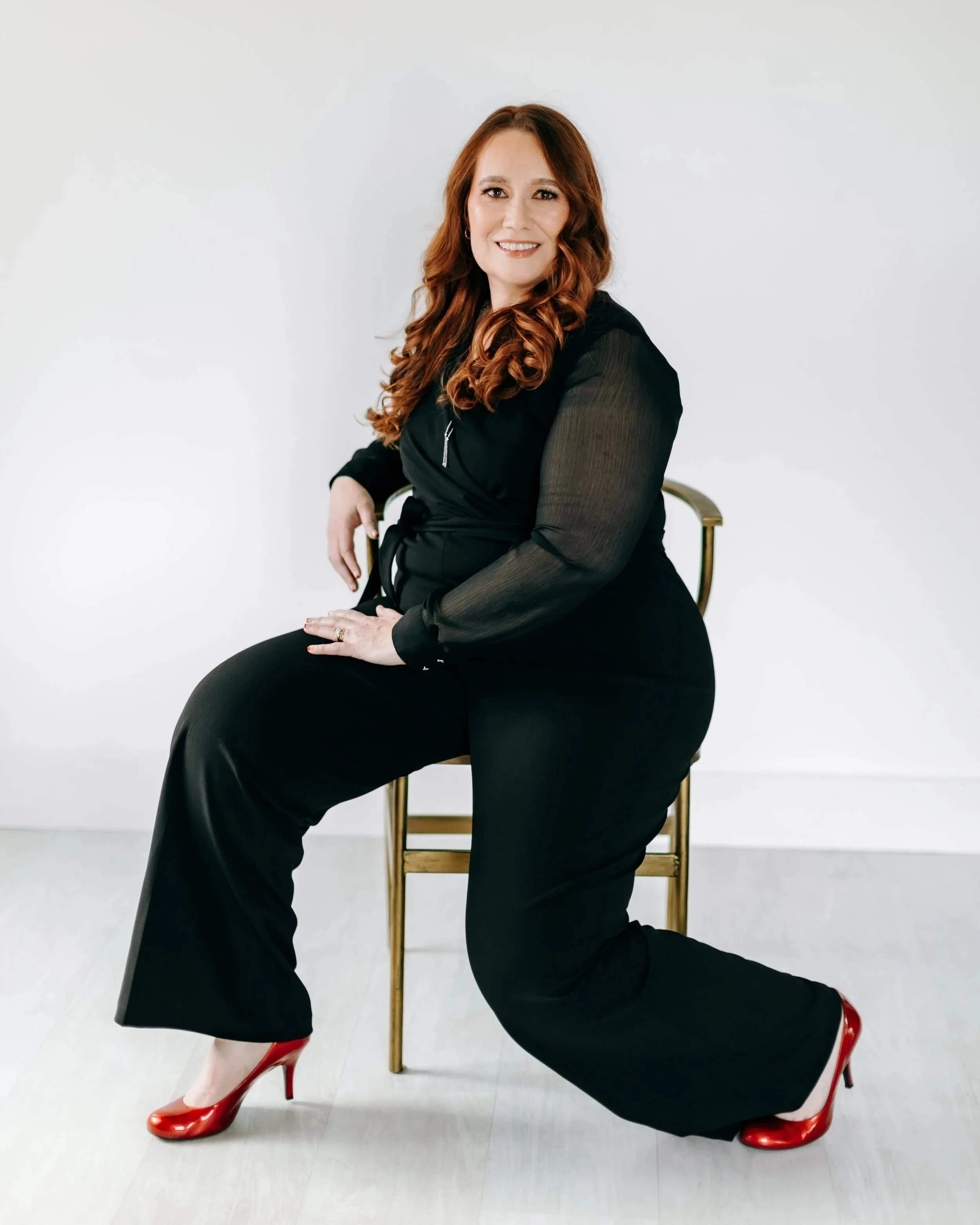 Bella in a chair with a black jumpsuit and red heels. Branding pictures.