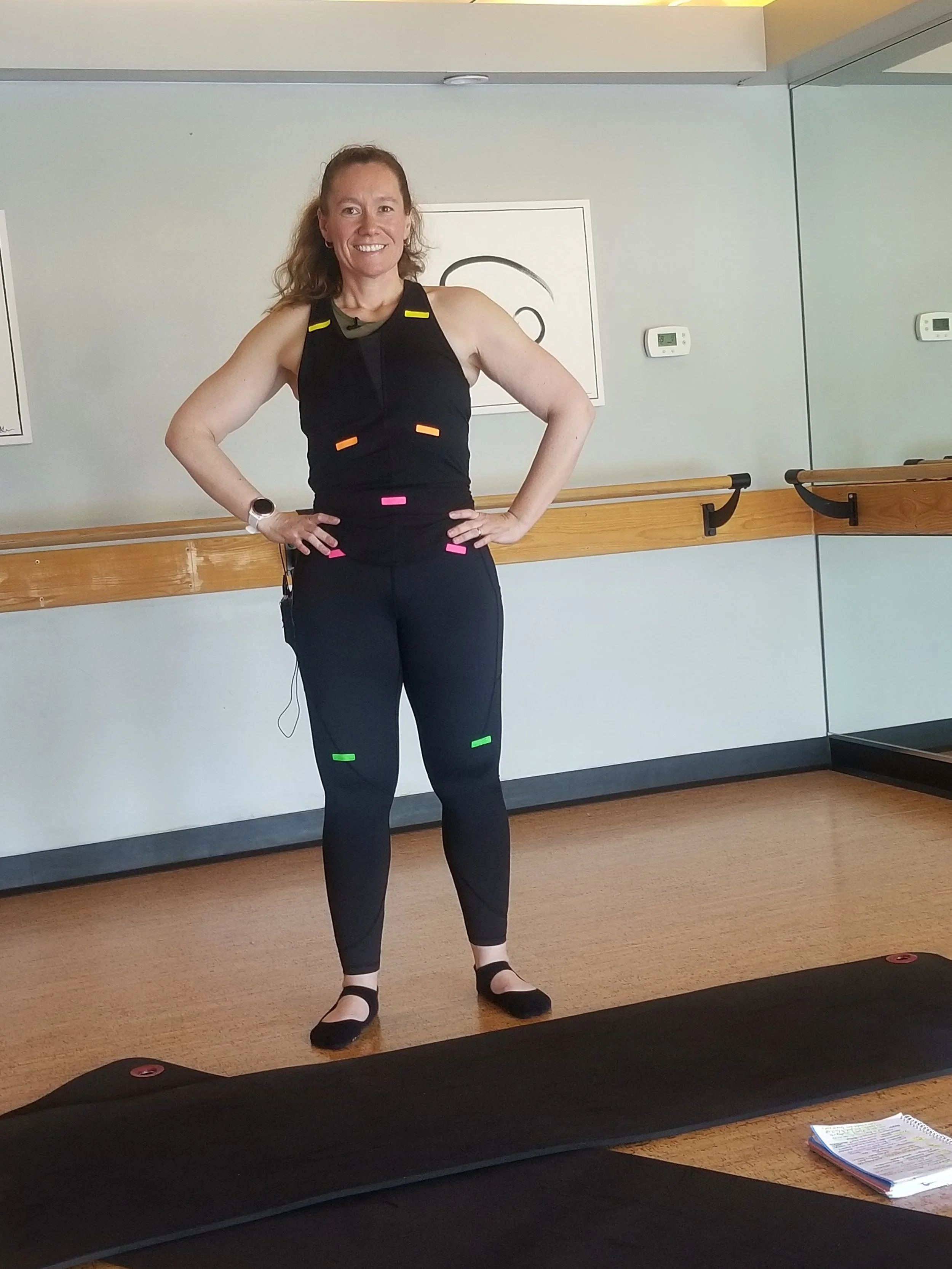Bella  demonstrating standing foundations of pilates with stickers on her body.