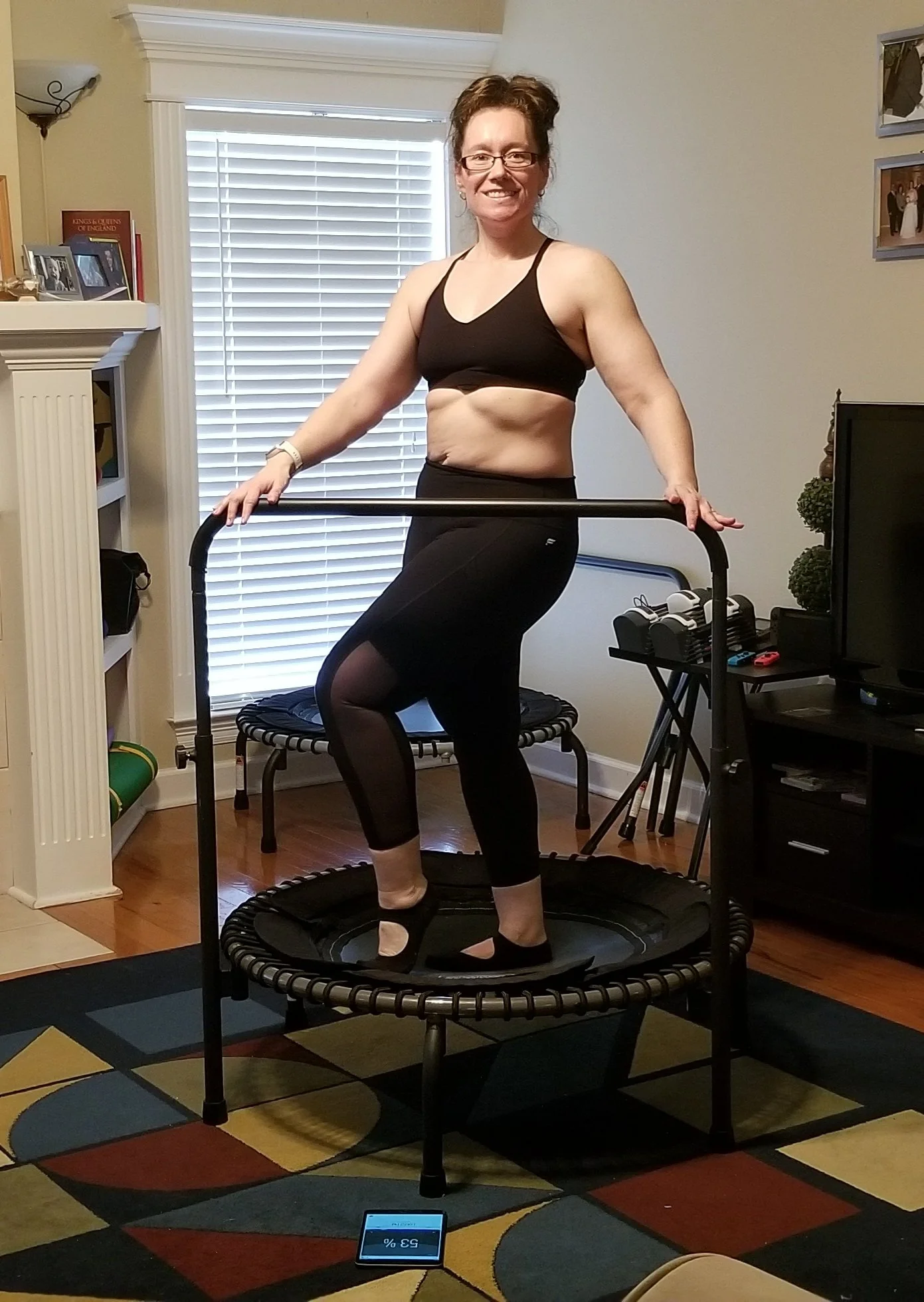 Woman with glasses wearing athletic clothing on a mini trampoline in a living room.