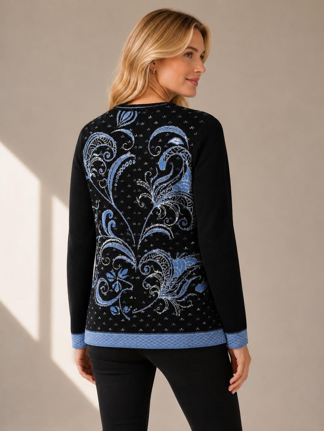Woman wearing a black alpaca sweater with blue floral artwork, hand-embroidered accents, and decorative metal clasps.jpg