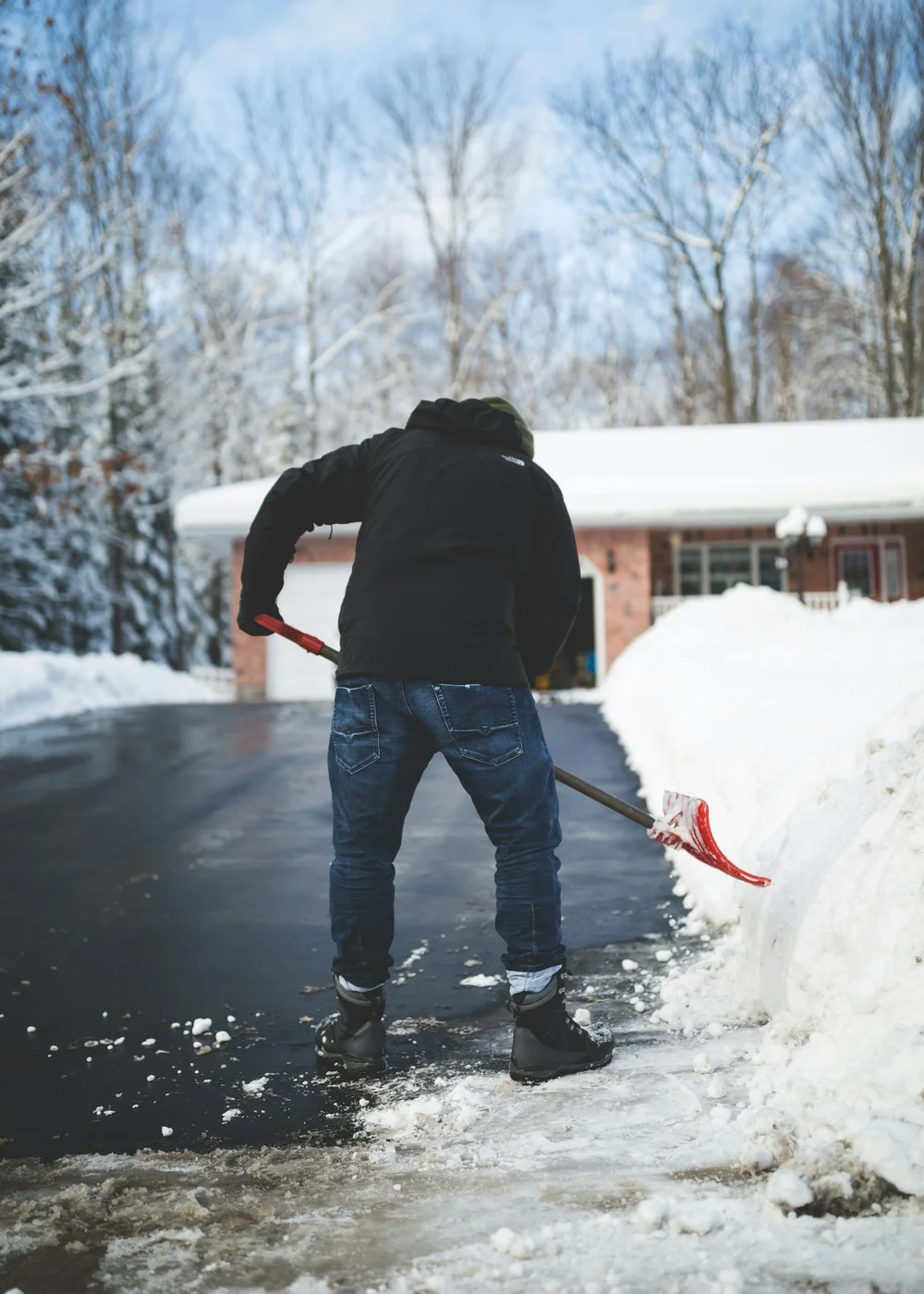 Person clearing snow from a residential driveway in front of a house on a snowy Ottawa day
