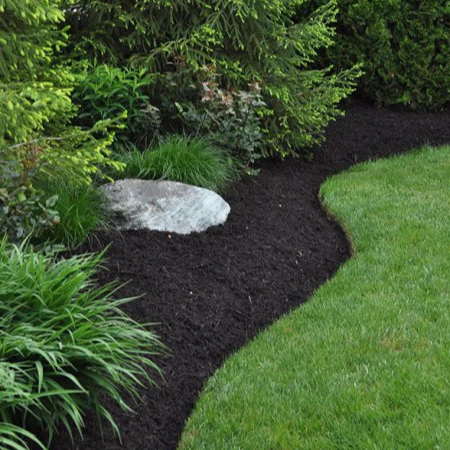 Freshly refreshed dark mulch garden bed bordered by green grass and plants