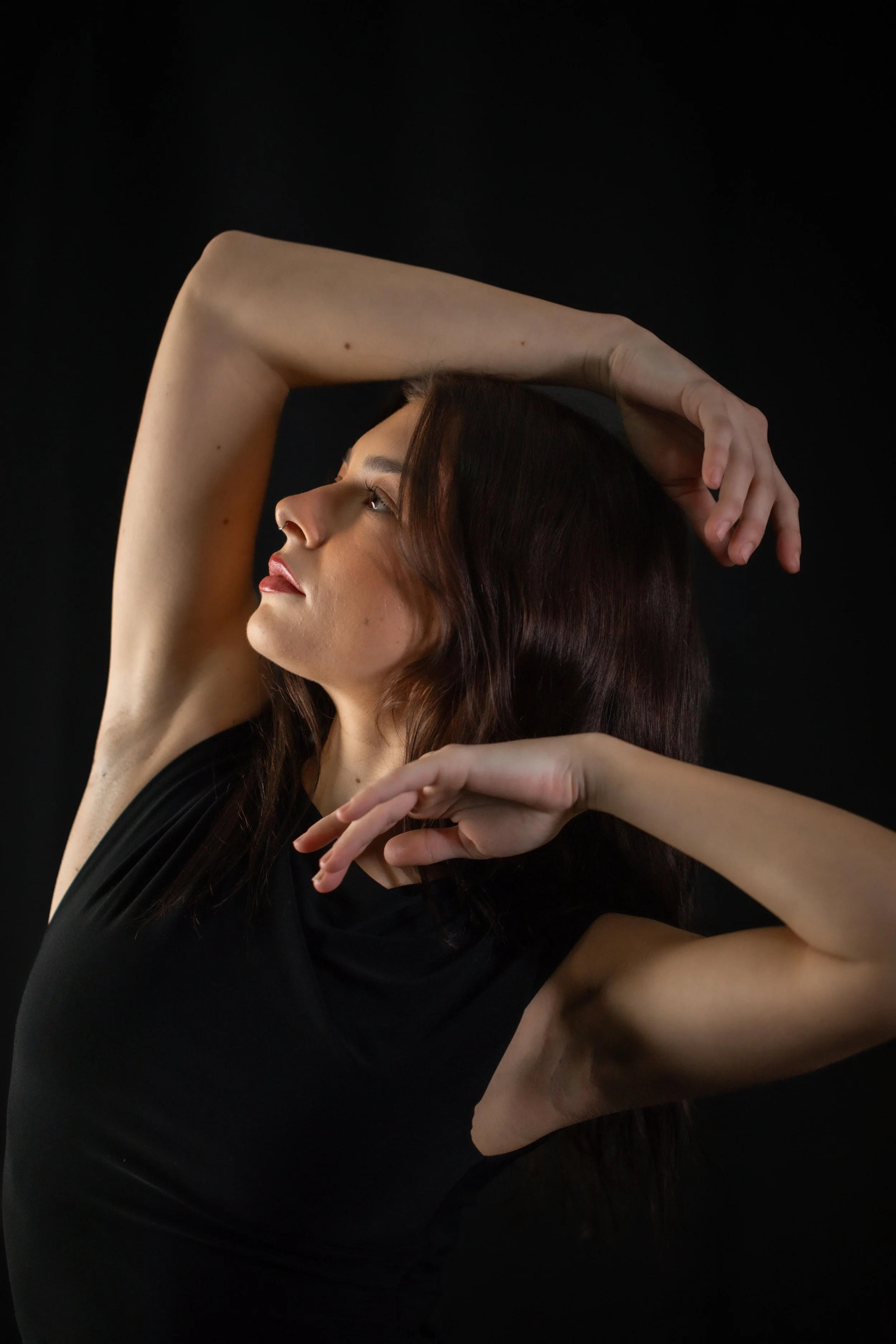 Black and white portrait of a woman with a thoughtful expression, hand under chin, wearing earrings and dark clothing.