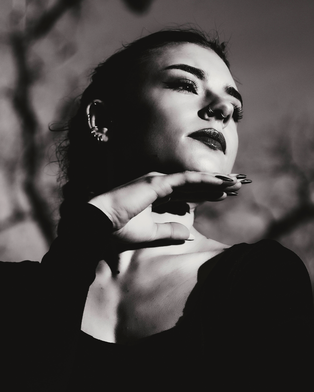 Black and white portrait of a woman with a thoughtful expression, hand under chin, wearing earrings and dark clothing.