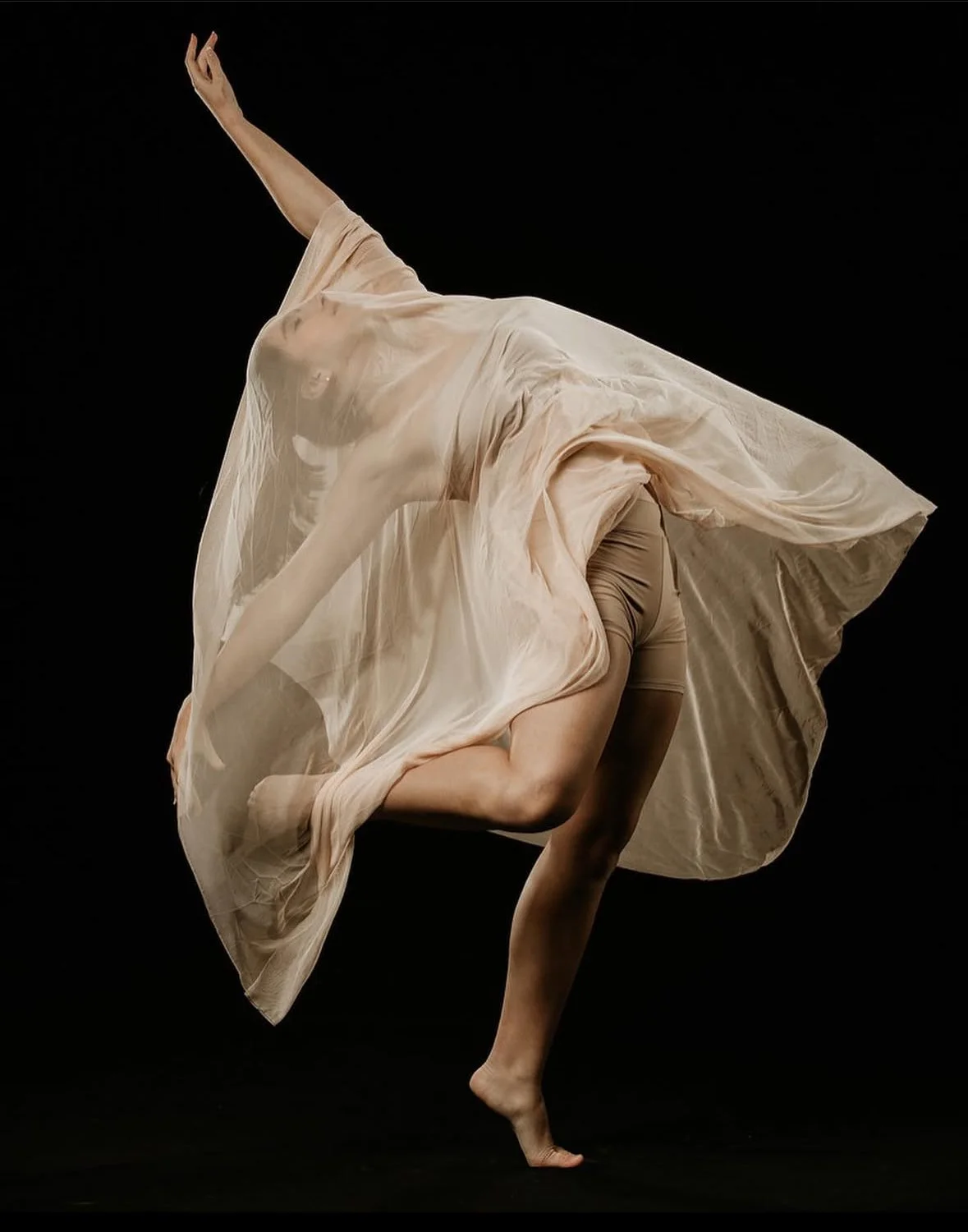 Dancer in motion with flowing fabric on dark background.