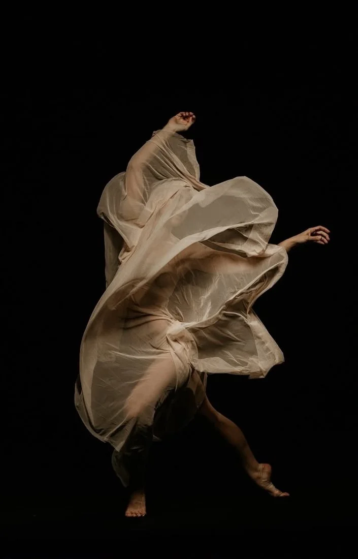 Dancer in motion with flowing fabric against a black background.