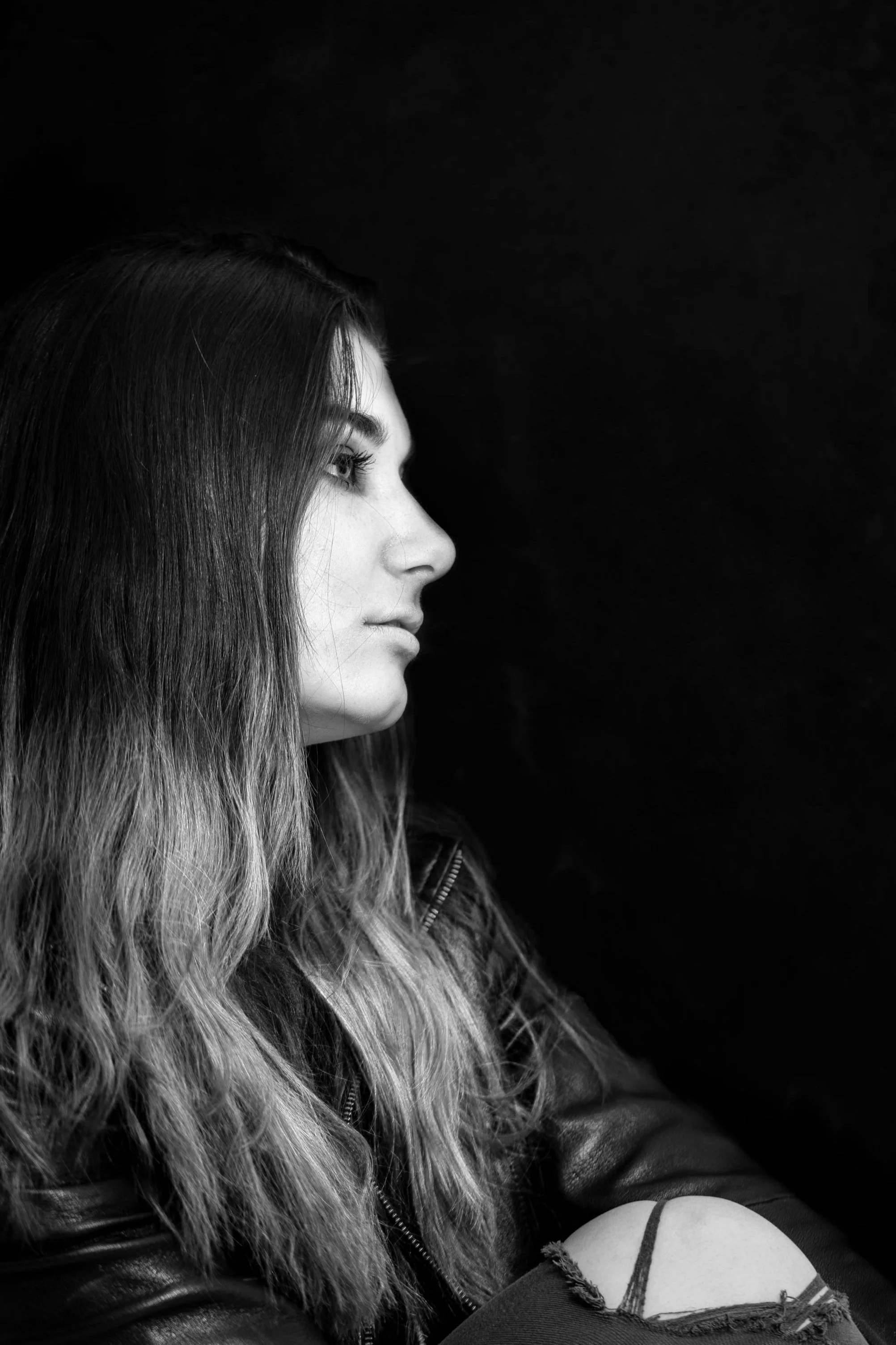 Black and white side profile of a woman with long hair and a leather jacket, gazing into the distance.