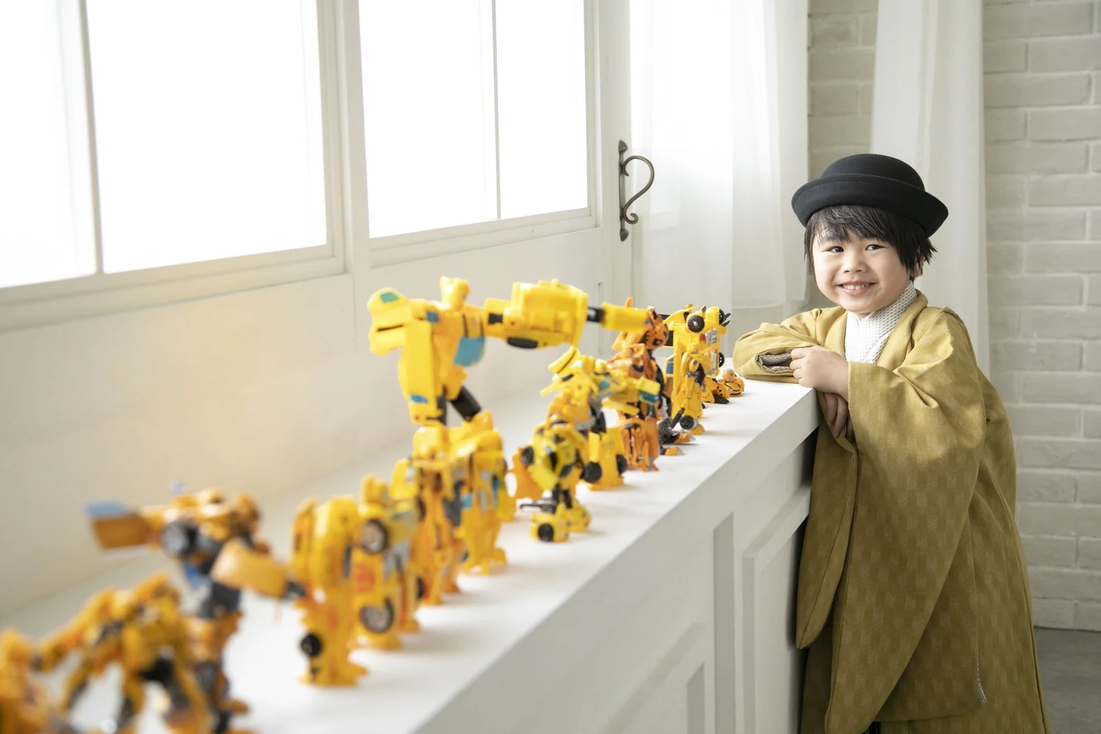 笑顔の少年が窓辺で黄色いロボット玩具を並べている