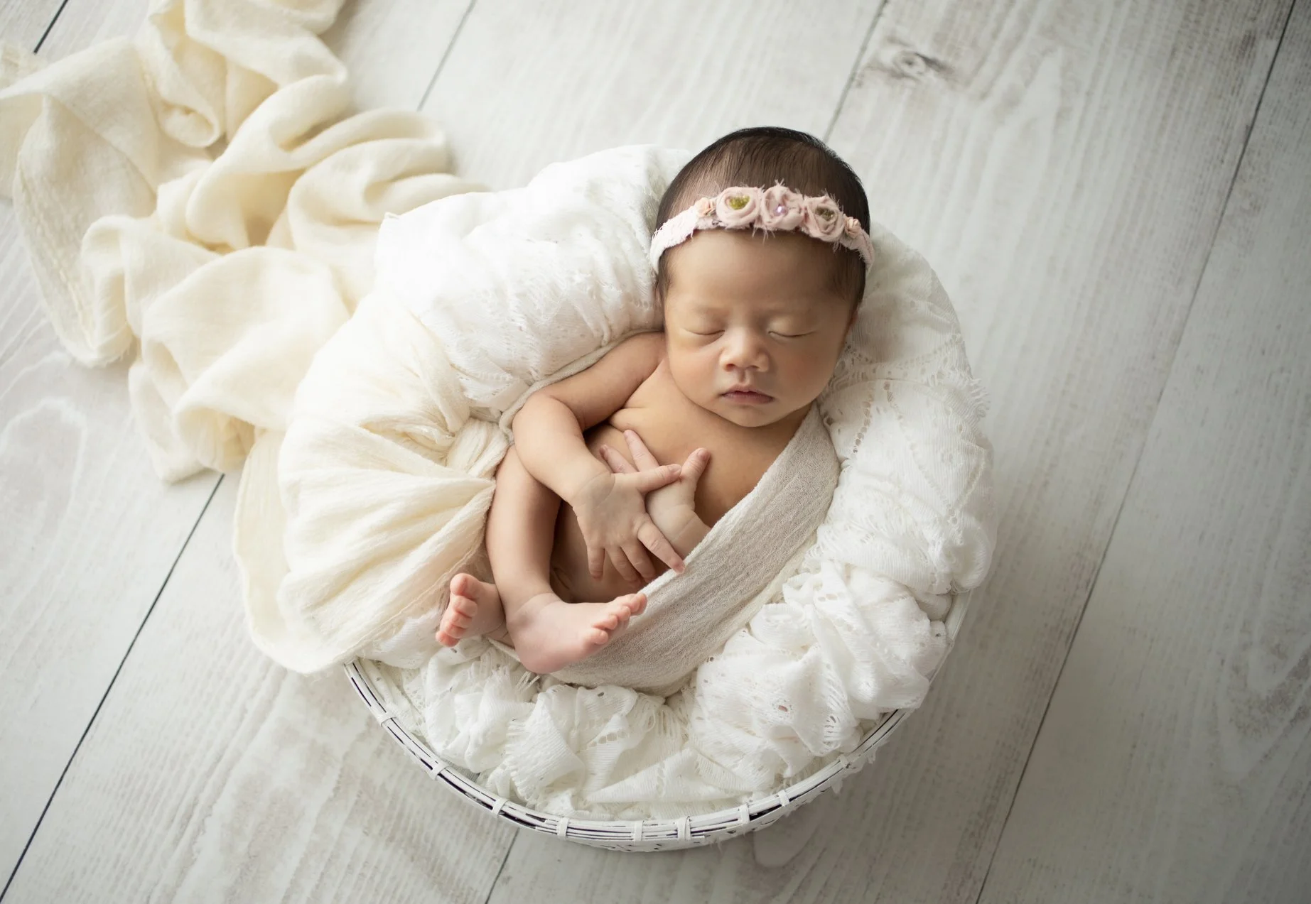 白いクッションの上に寝ている赤ちゃん。頭に花の飾りがついたヘアバンドをつけている。