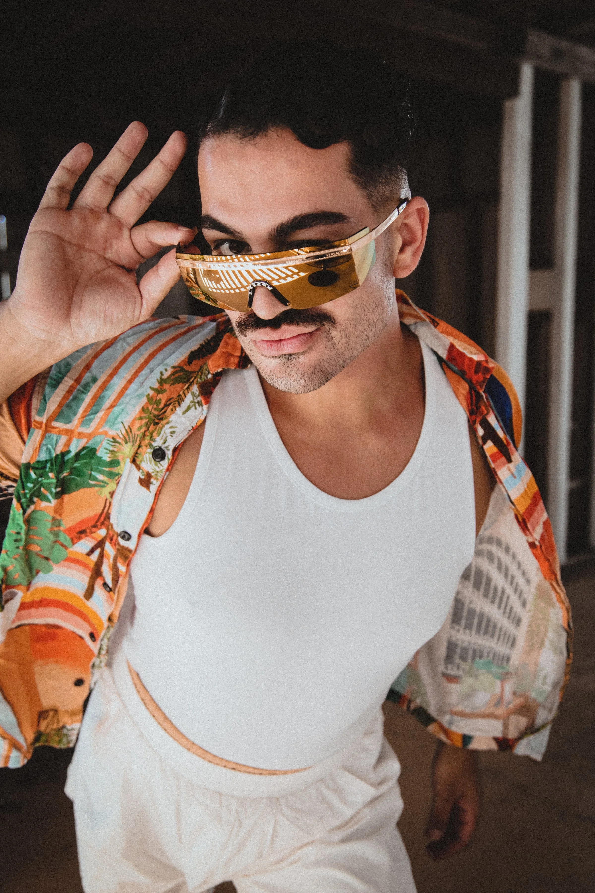 Person wearing a colorful shirt, white tank top, and reflective sunglasses, posing confidently.