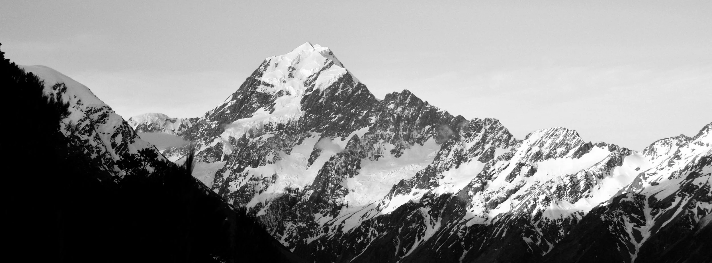 Black and white photo of snow-capped mountain peaks, clear sky.