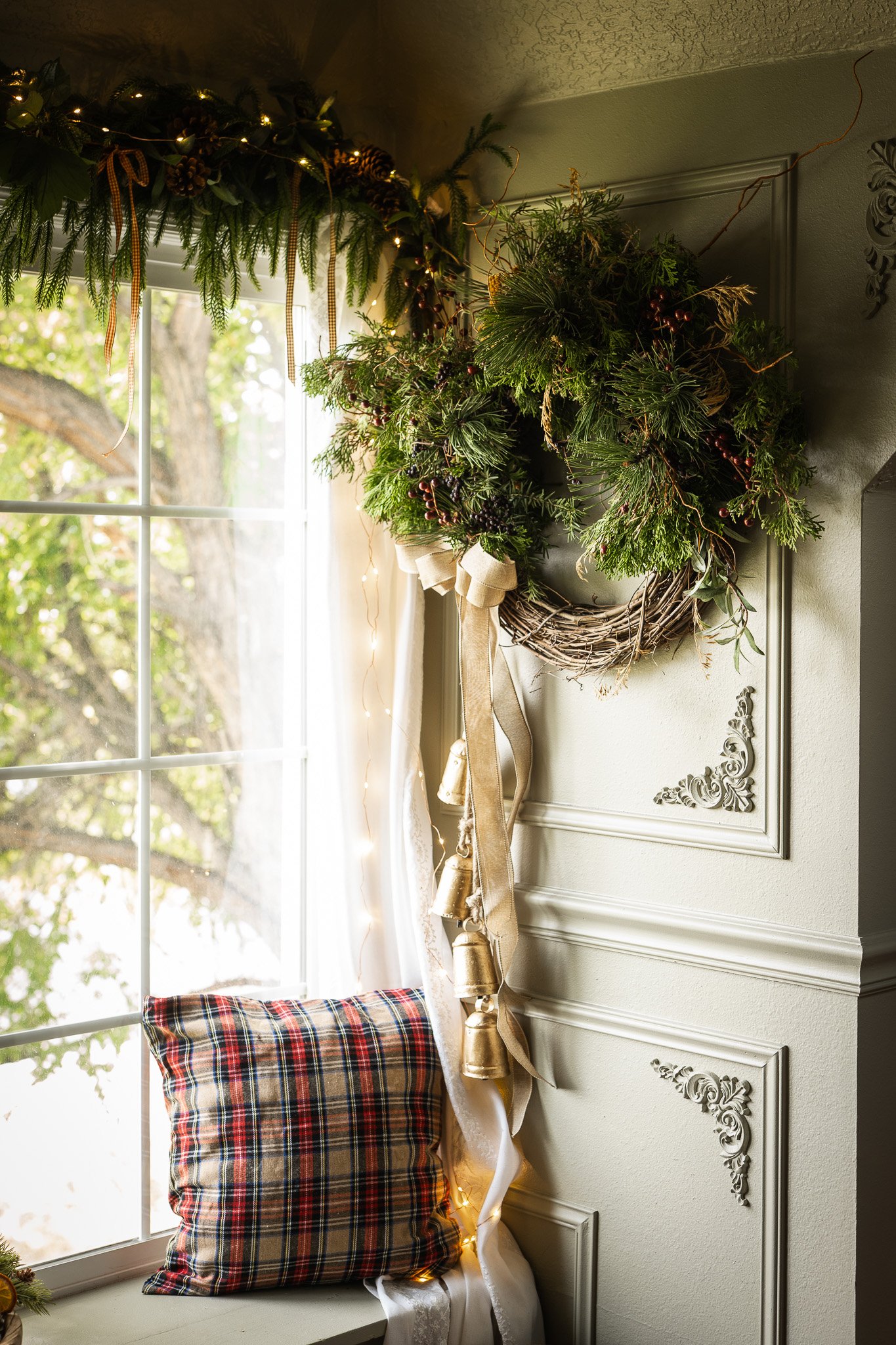 Decorated window ledge with Christmas greenery, string lights, a plaid pillow, and a wreath hanging on the wall.