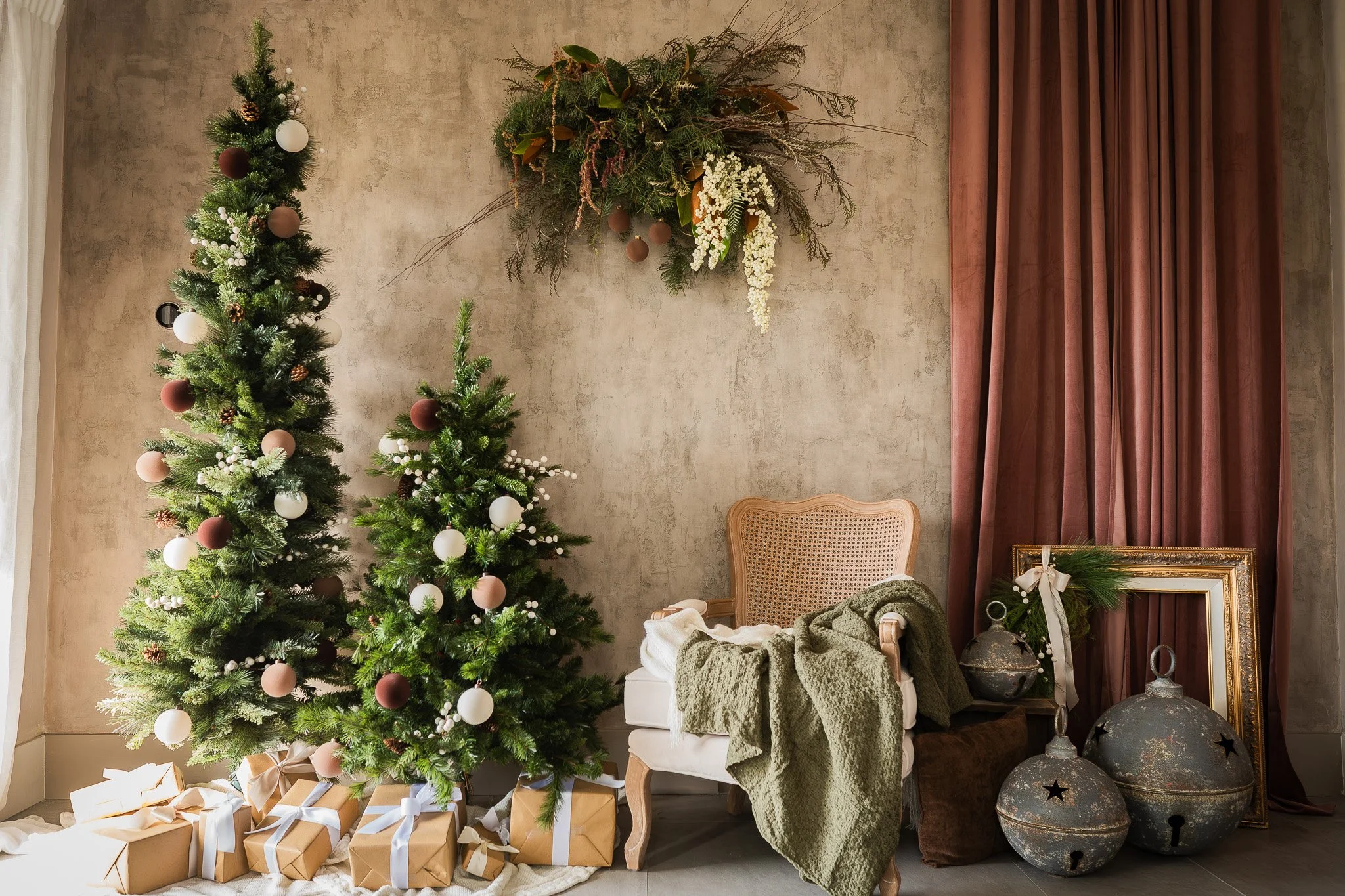 Christmas scene with decorated Christmas tree, wrapped presents, a vintage-style chair with blanket, and holiday decorations including metallic ornaments, picture frame, and a floral arrangement hanging on the wall.