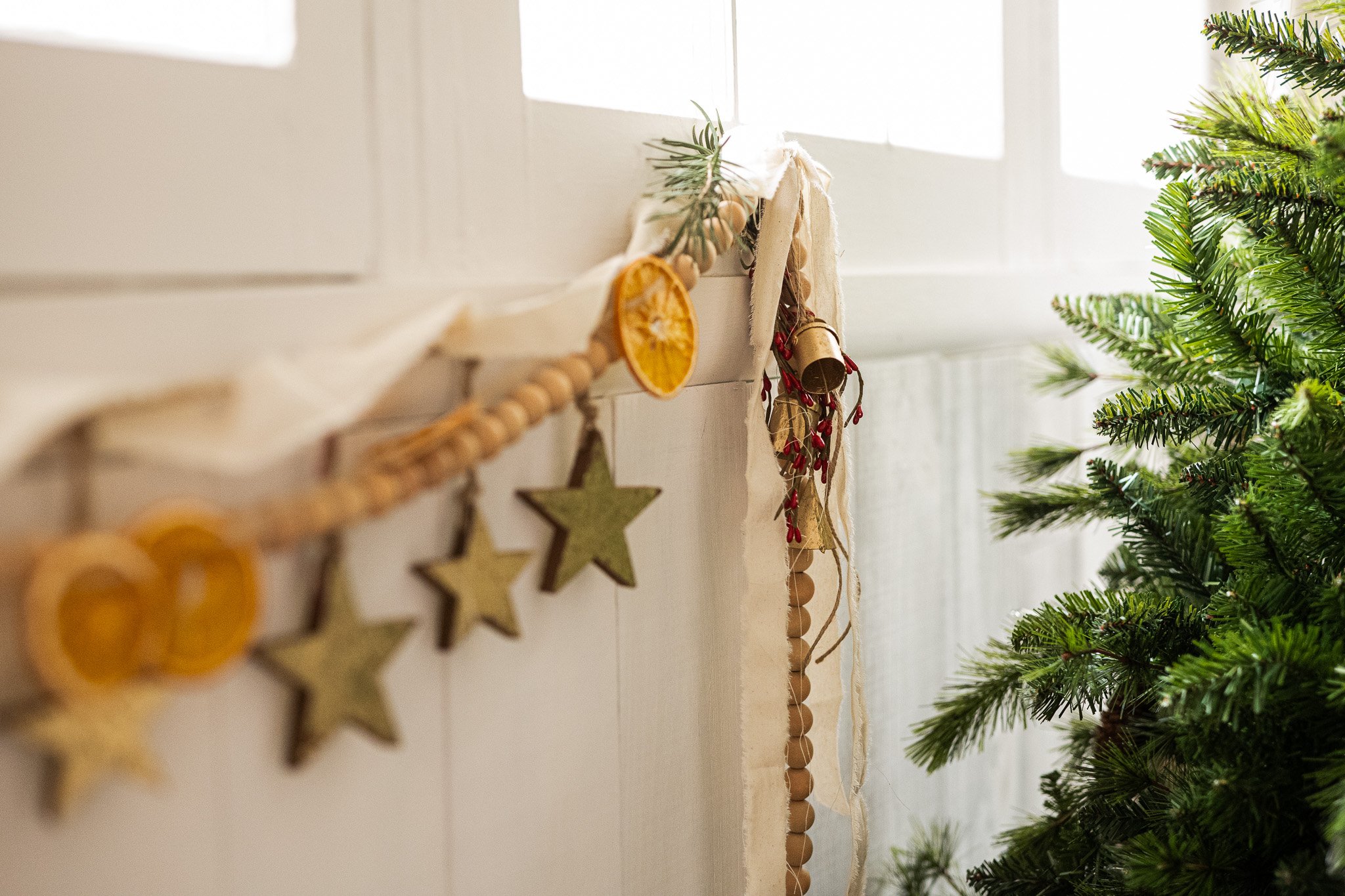 Close-up of a decorated Christmas tree next to a white wall with hanging holiday ornaments and dried citrus slices.