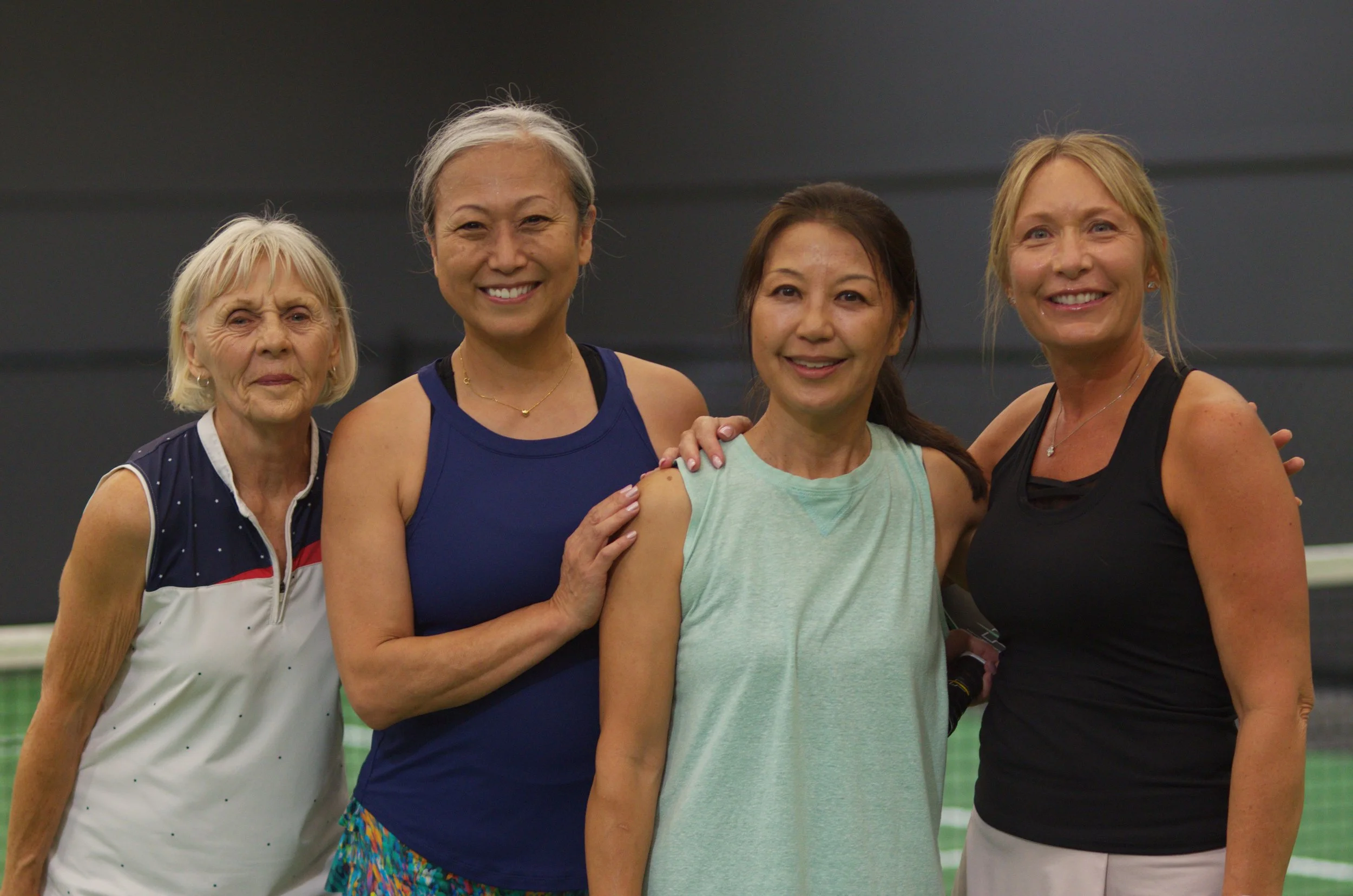 Four women posing on a pickleball court