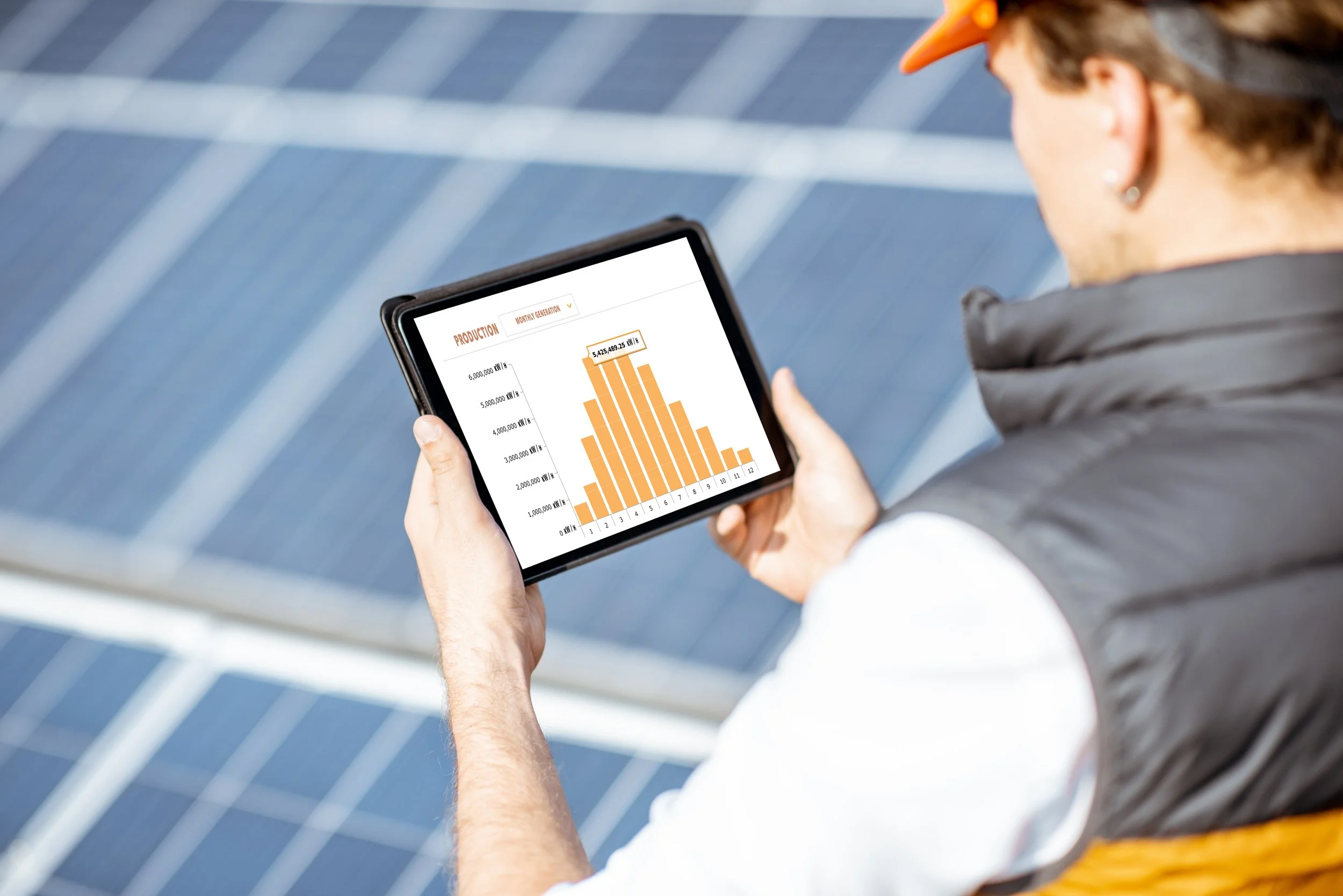 Person viewing solar energy data on a tablet near solar panels.