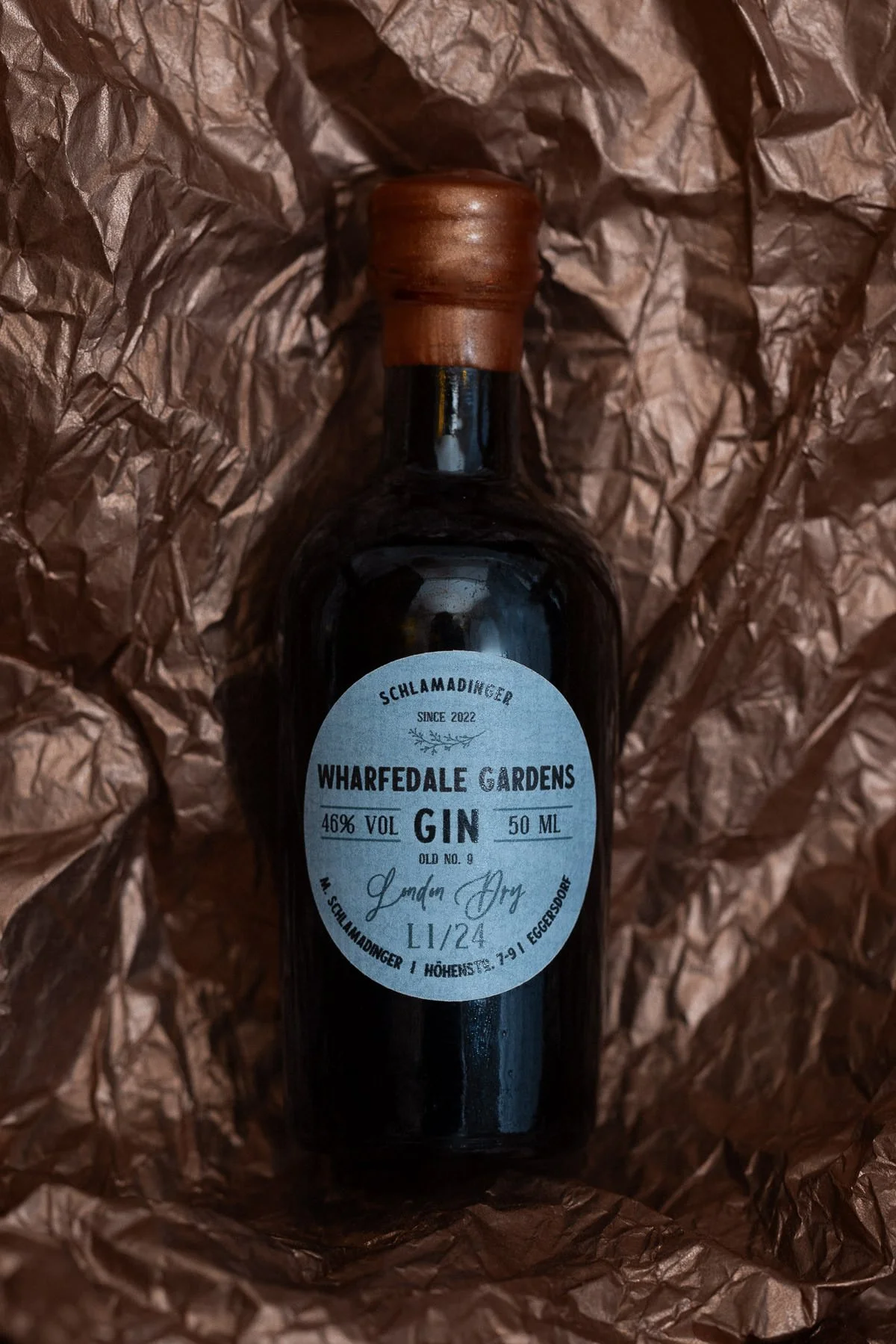 Schwarze Gin-Flasche mit Holzverschluss, umgeben von braunem, zerknittertem Papier.
