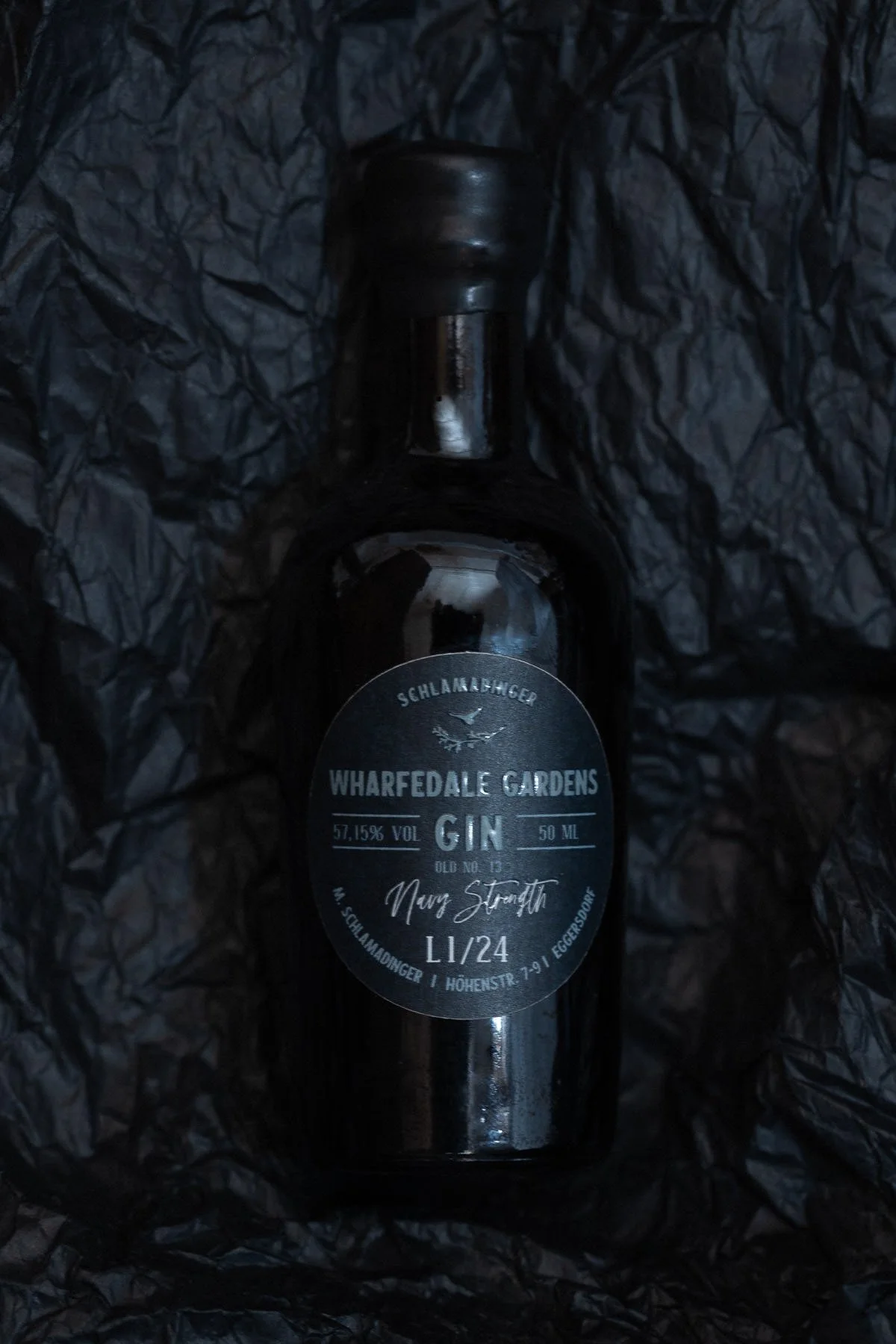 Flasche mit schwarzem Etikett, liegt auf schwarzem Papier