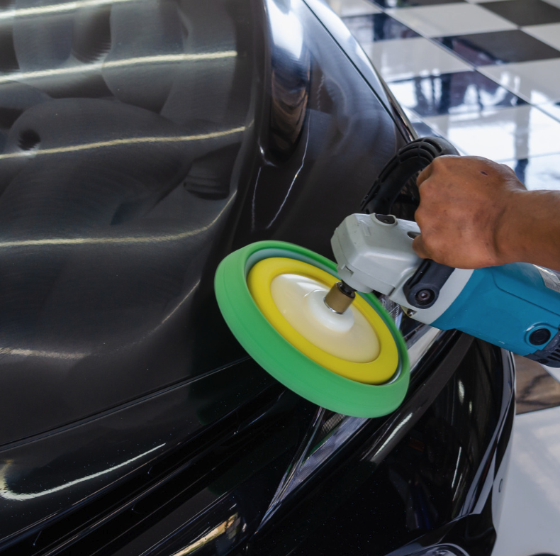 Person using a buffer machine on a black car surface