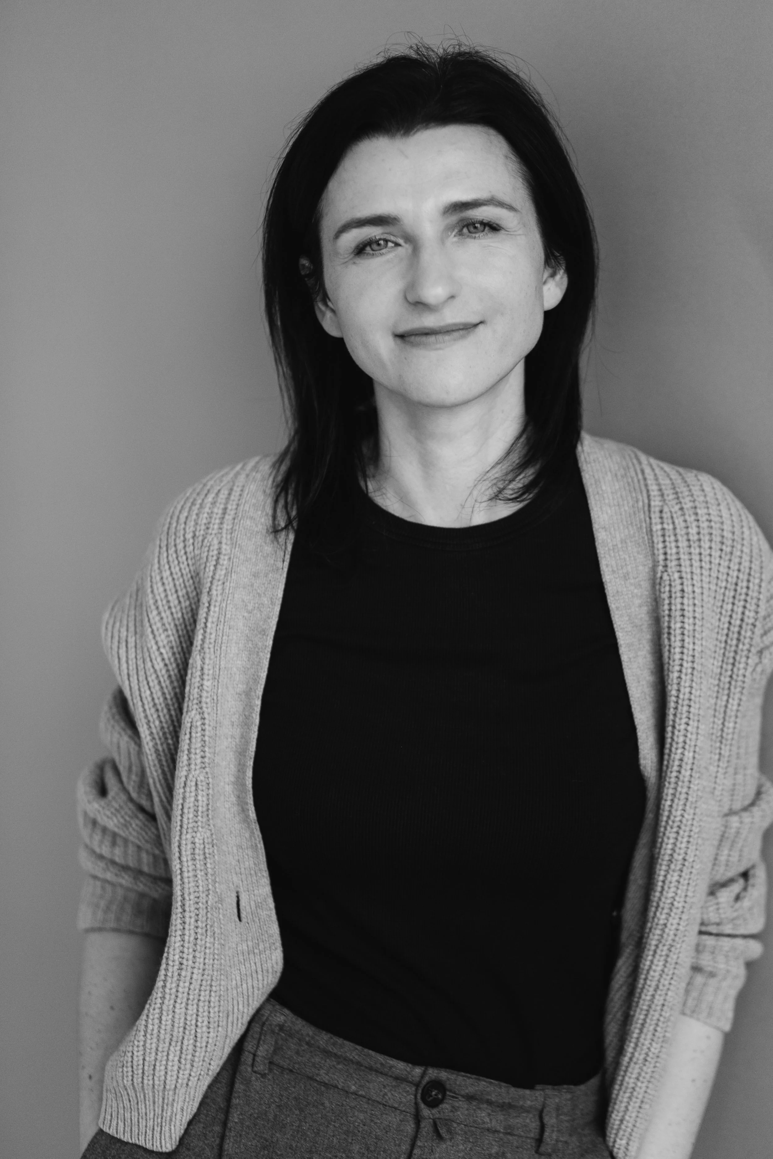 Schwarz-weiß-Foto von Maria Kopp, einer lächelnden Frau mit dunklem Haar, die einen Pullover und ein dunkles Shirt trägt. Sie schaut direkt in die Kamera.