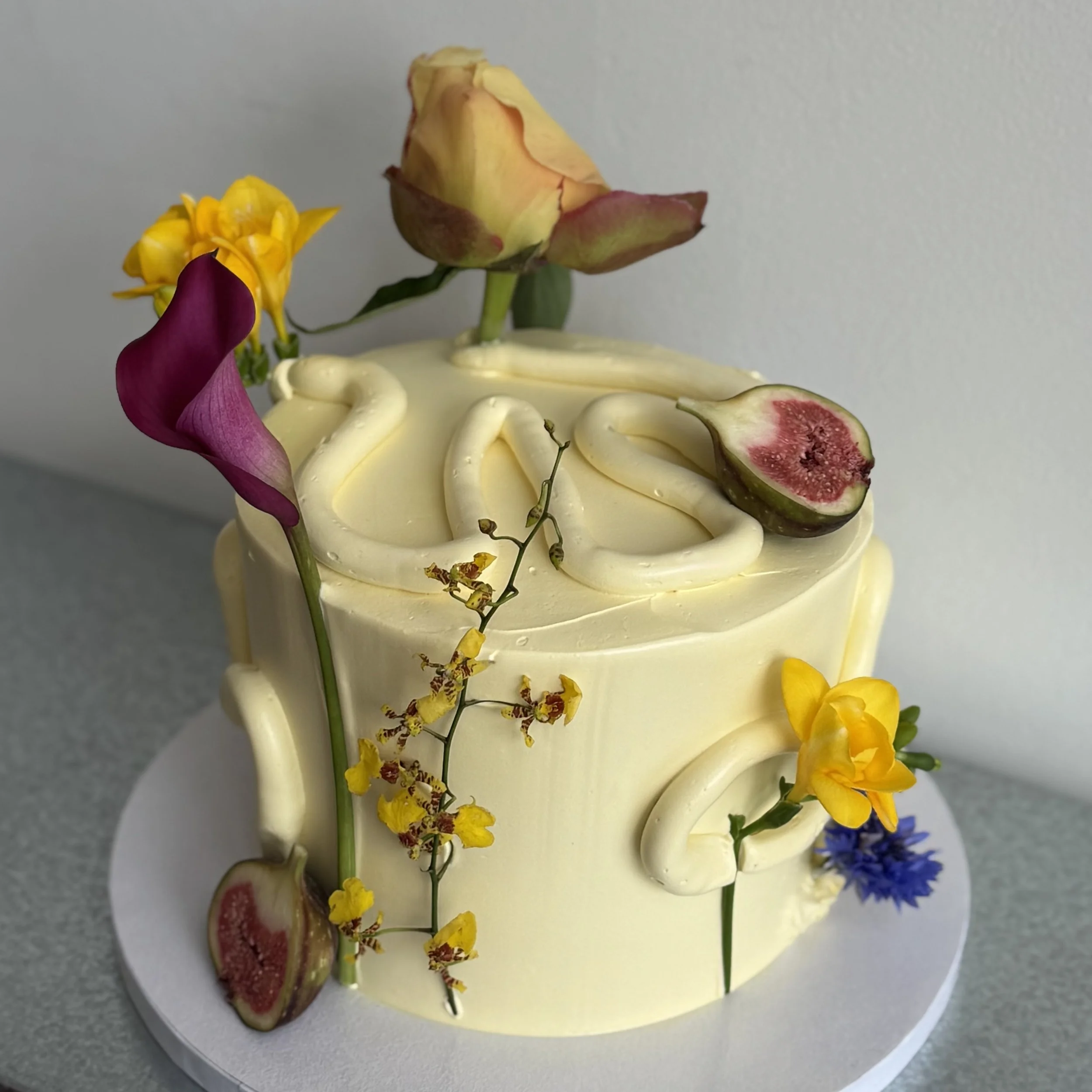 A round cake decorated with fresh flowers and fruit slices.