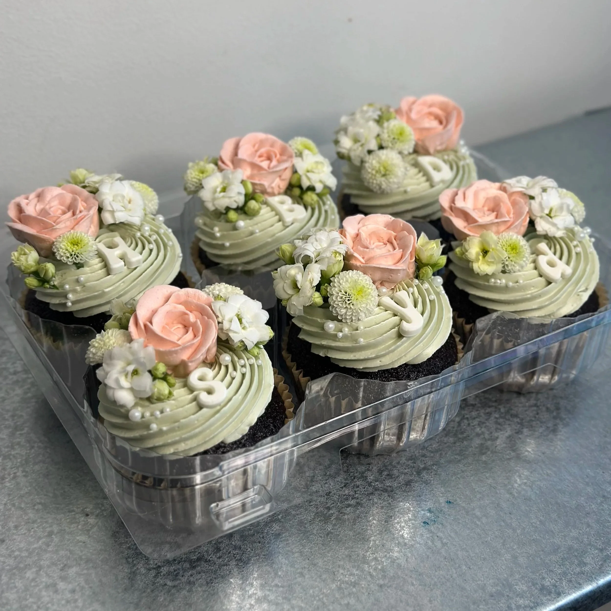 Set of decorated cupcakes with light green frosting, pink roses, white flowers, and small white pearl decorations.