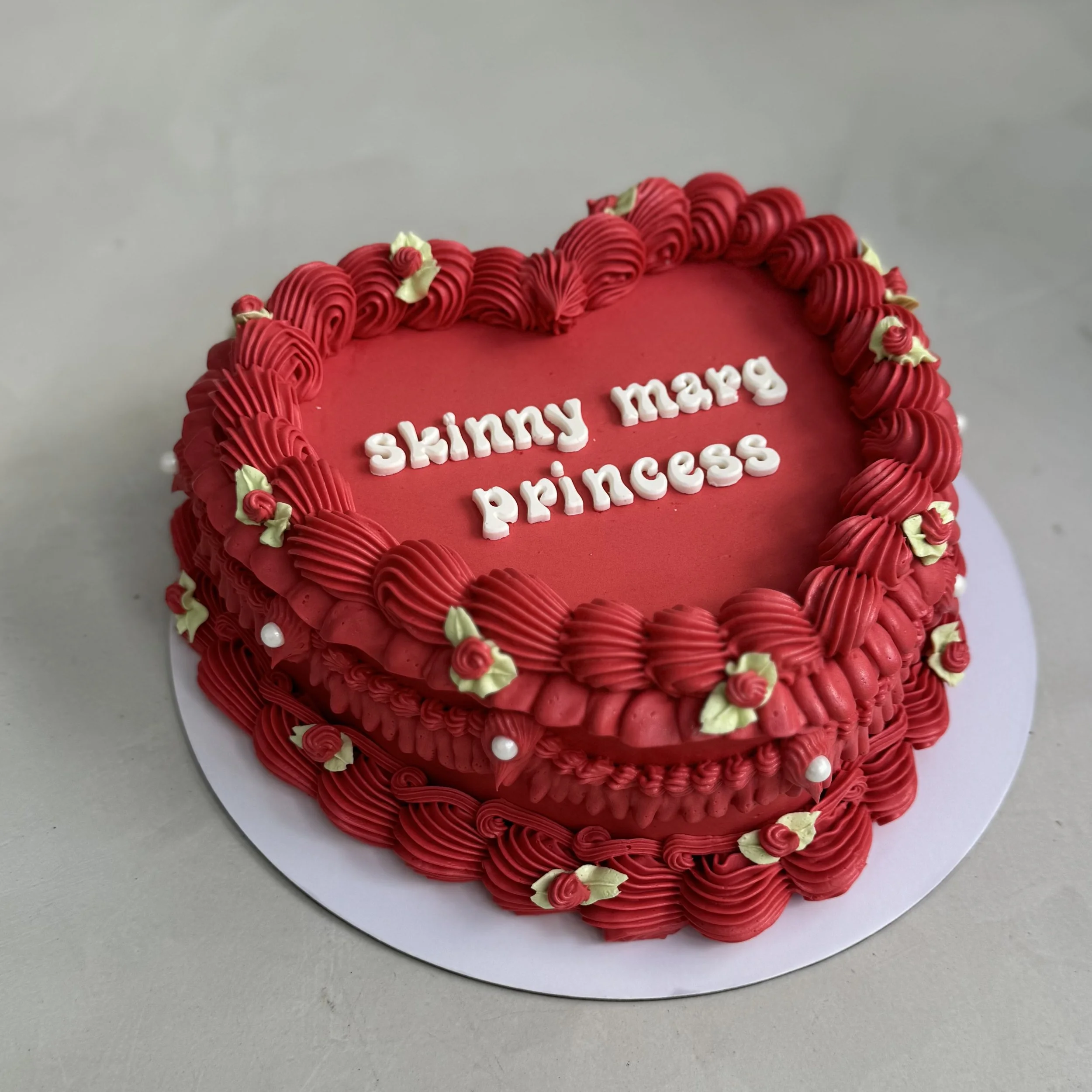 Red heart-shaped cake with pink and white icing decorations and the words "skinny mama princess" written in white icing on top.