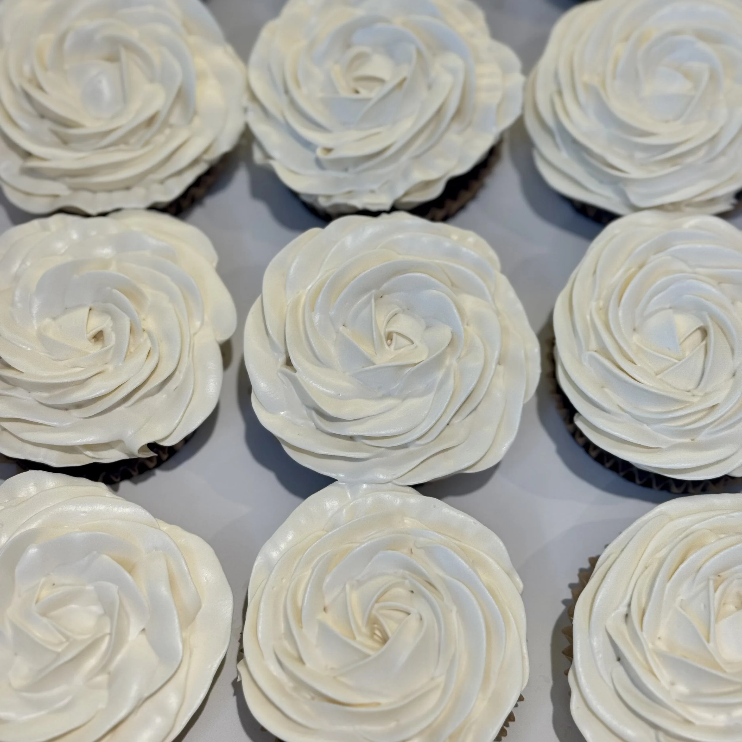 Nine cupcakes topped with white buttercream frosting piped in a rose pattern.