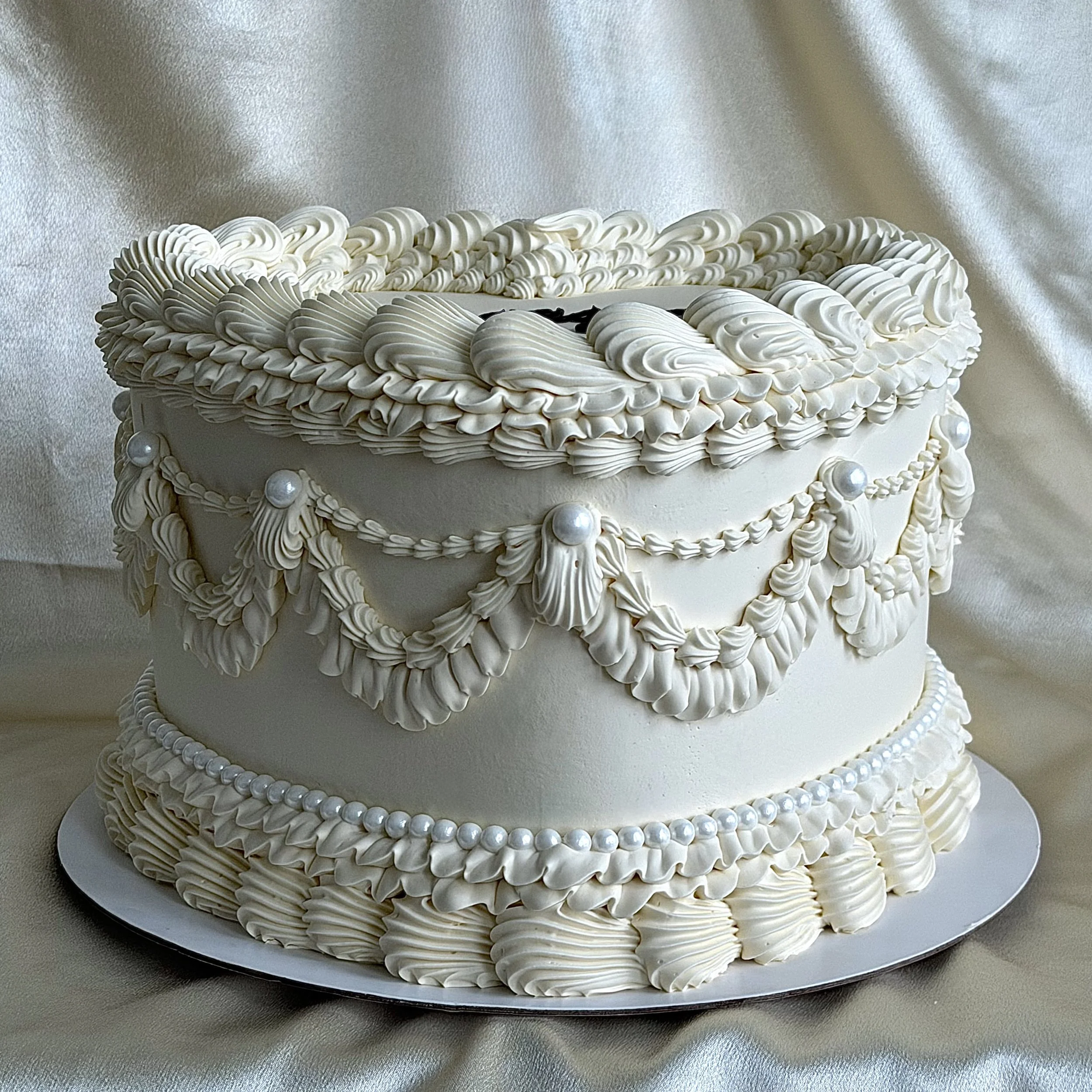 A white heart-shaped cake decorated with piped white frosting and the word 'engaged' written in black icing on top.