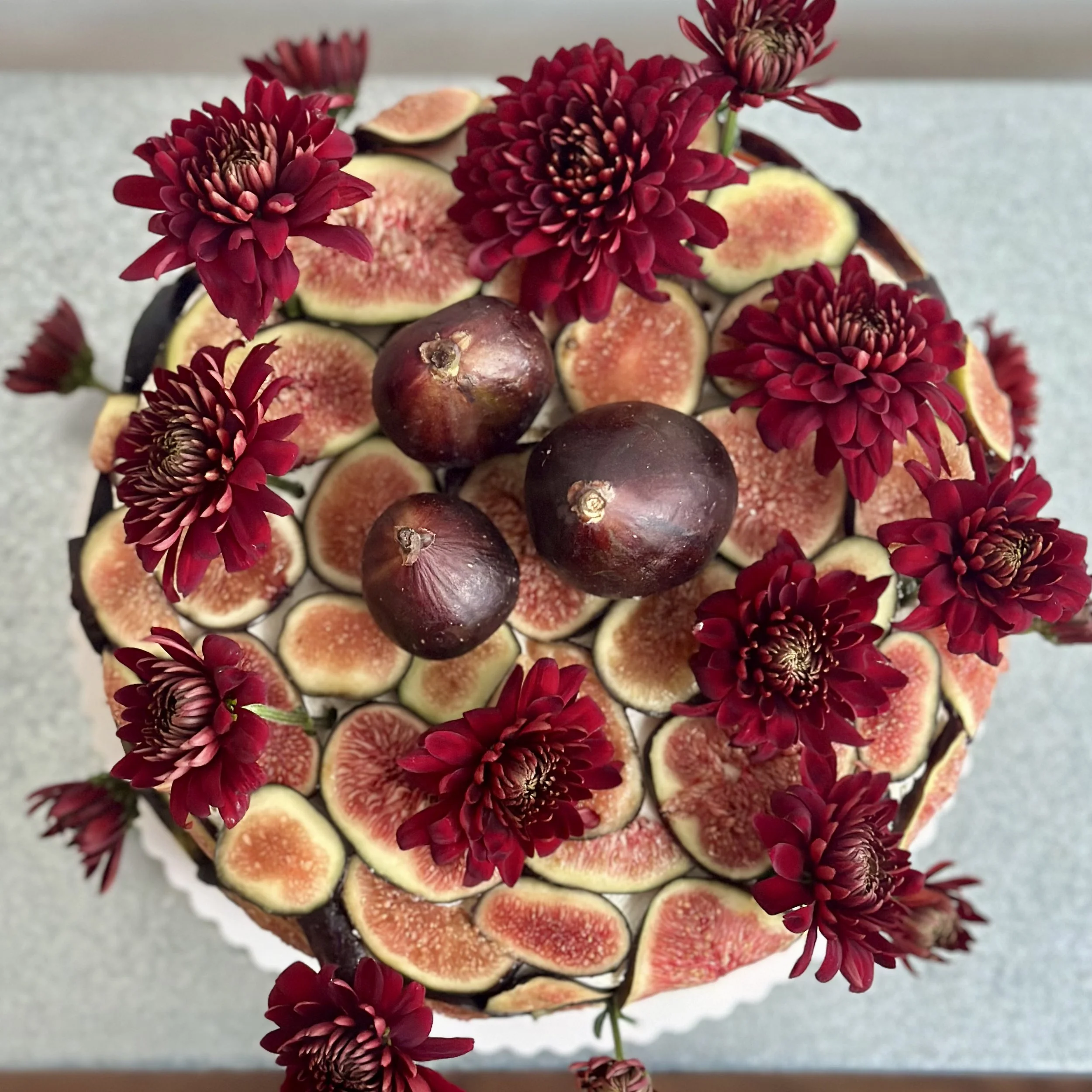 Top view of a cake decorated with sliced figs, dark cherries, and deep red flowers.