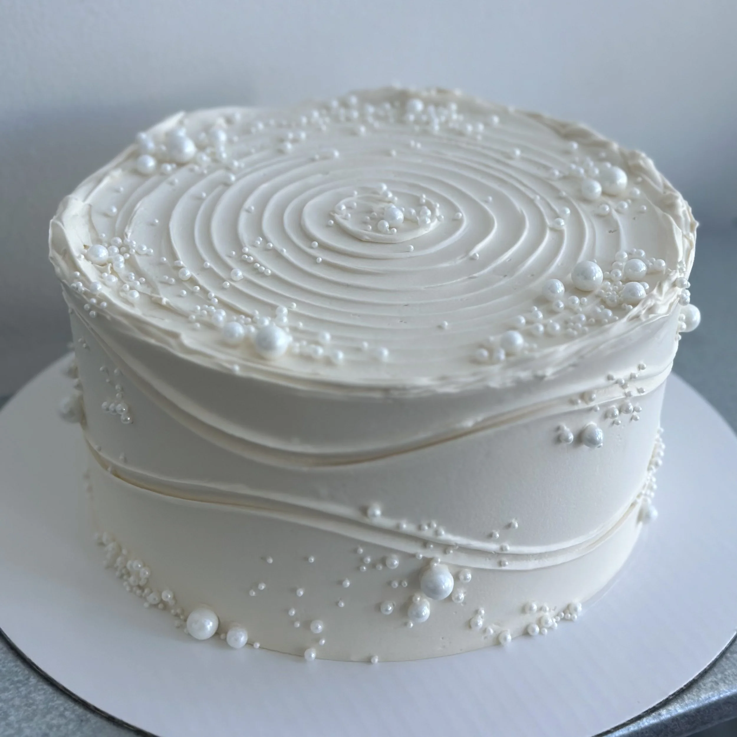 A heart-shaped white cake decorated with white pearls and swirls of white icing.