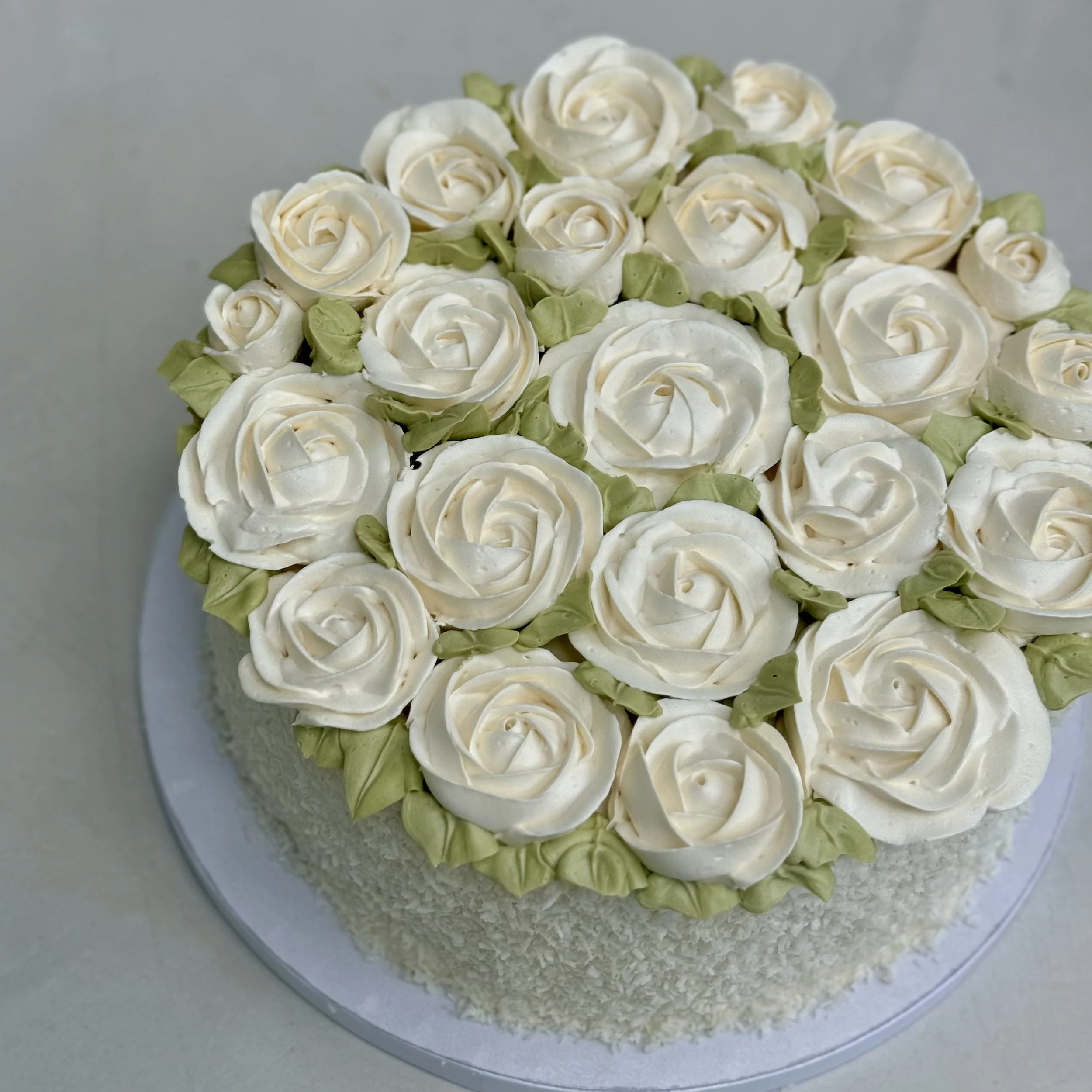 Round cake decorated with white rose-shaped frosting and small green frosting leaves.