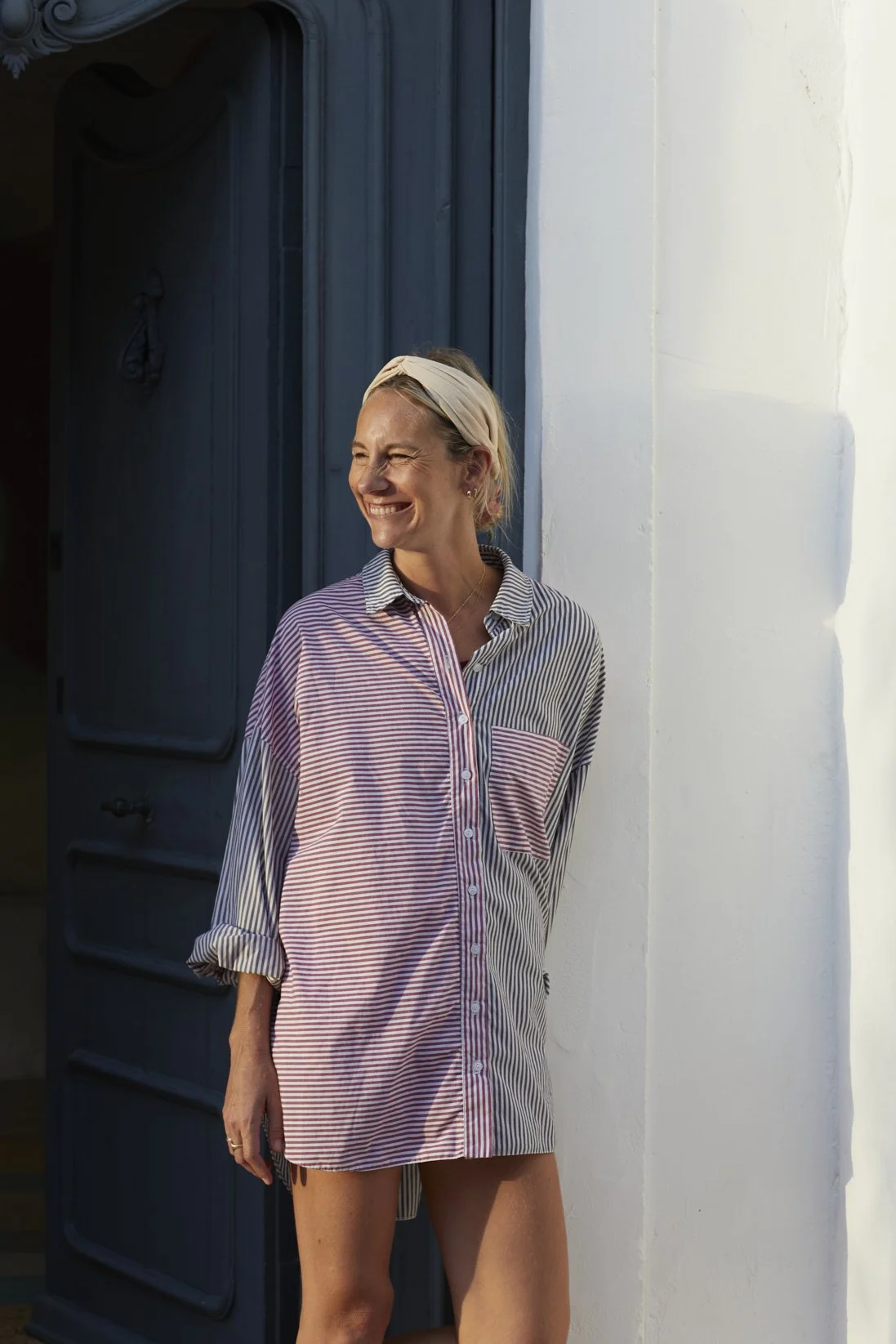 Jocie smiling, wearing a striped shirt, standing by a door and white wall.