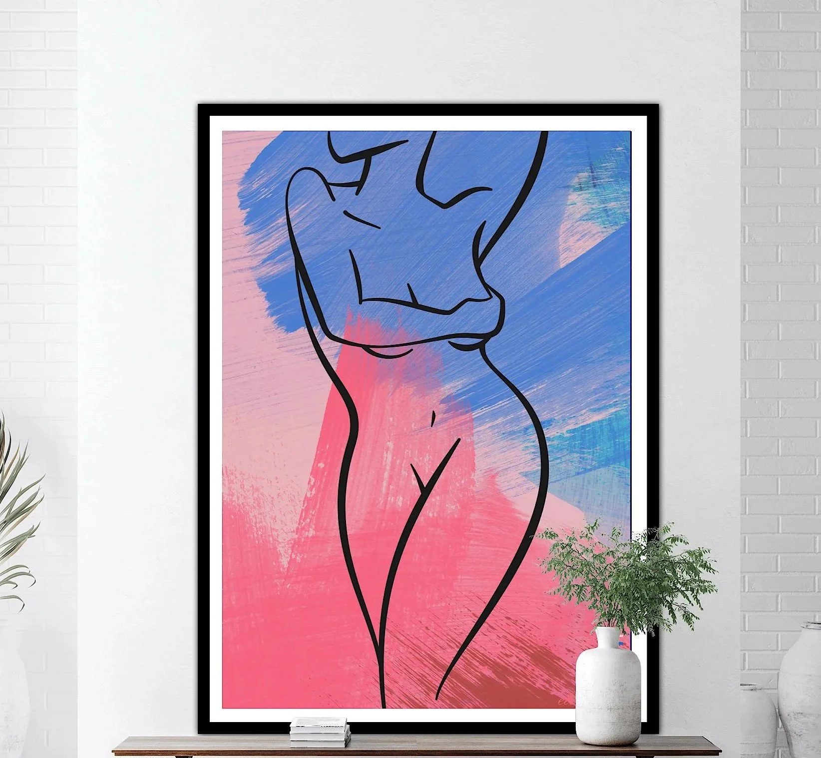Abstract artwork of a woman with black outline, colorful pink and blue background, framed and displayed on a white wall with plants nearby.