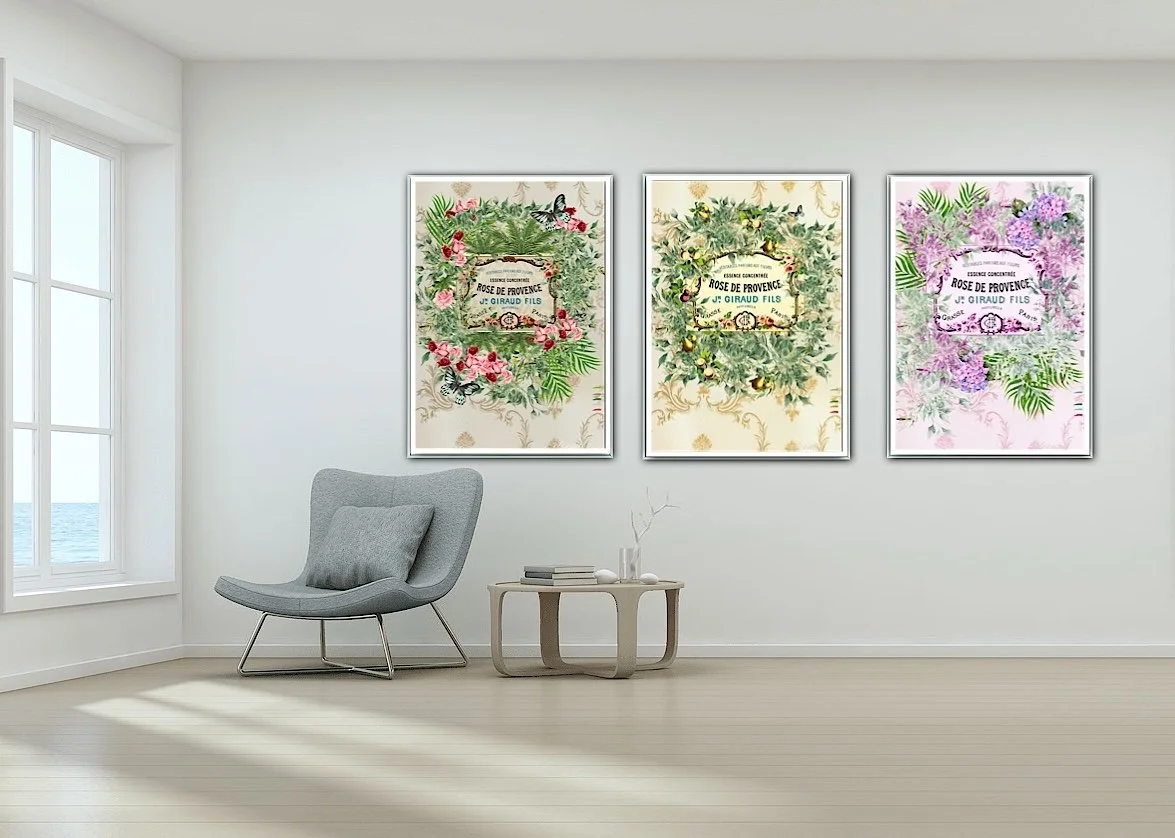 Three floral paintings hanging on a white wall in a bright, modern living room with a gray armchair and a small wooden table with books and decorative branches.